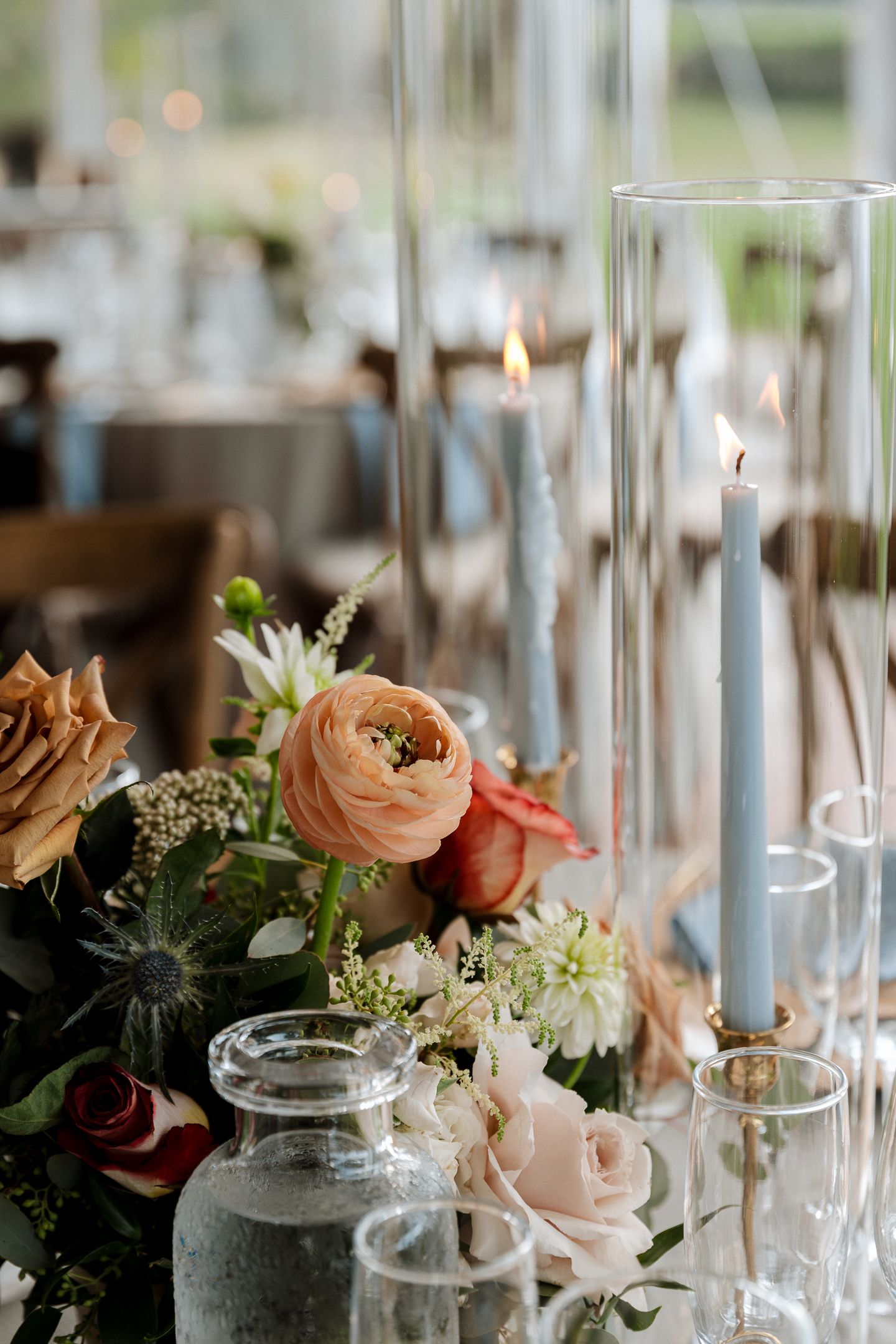 Elegant wedding table with blue taper candles in glass holders, peach ranunculus, roses, and greenery centerpiece.