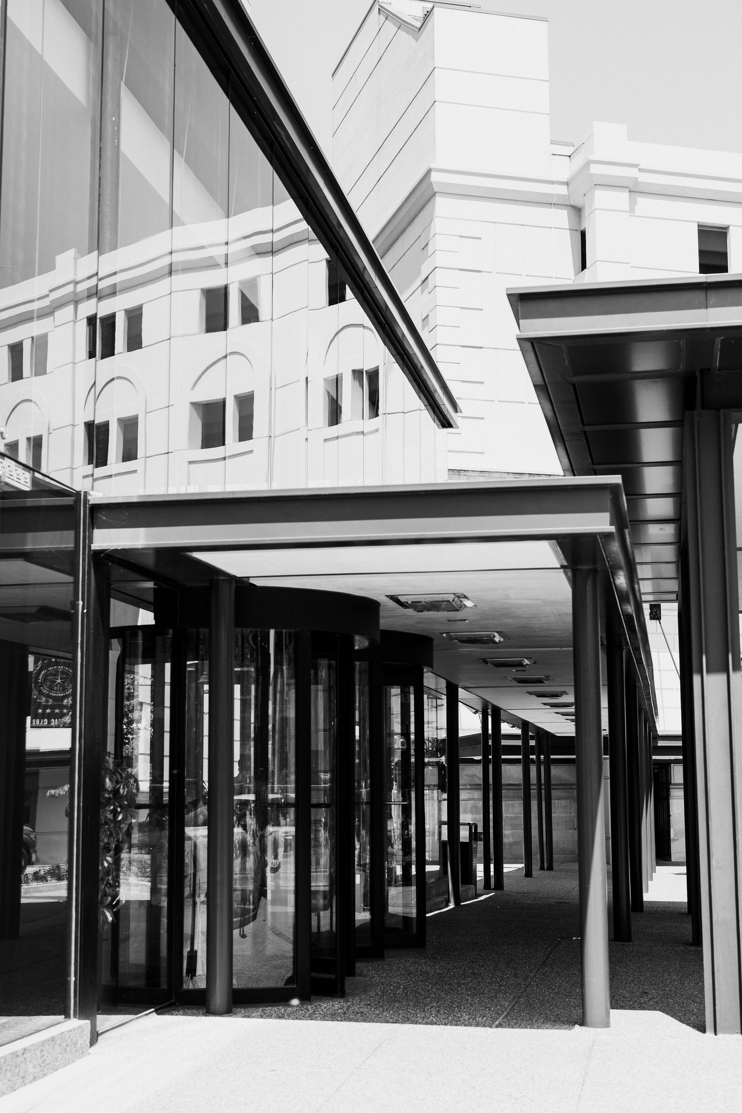 Black and white photo of a modern building entrance with revolving doors and glass facade.