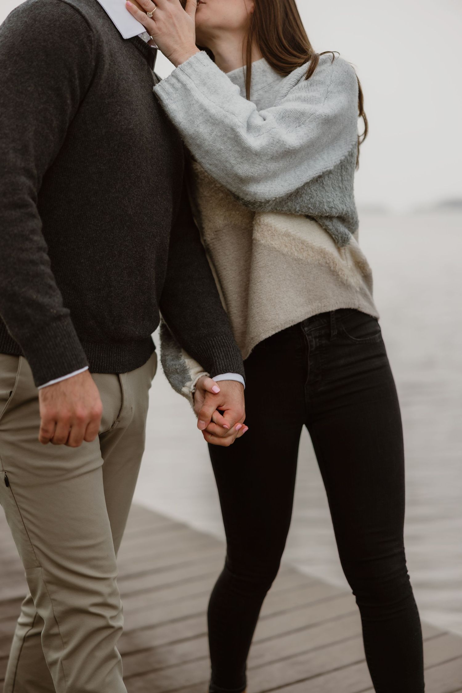 A couple holds hands and shares a kiss on a wooden dock on a misty day.