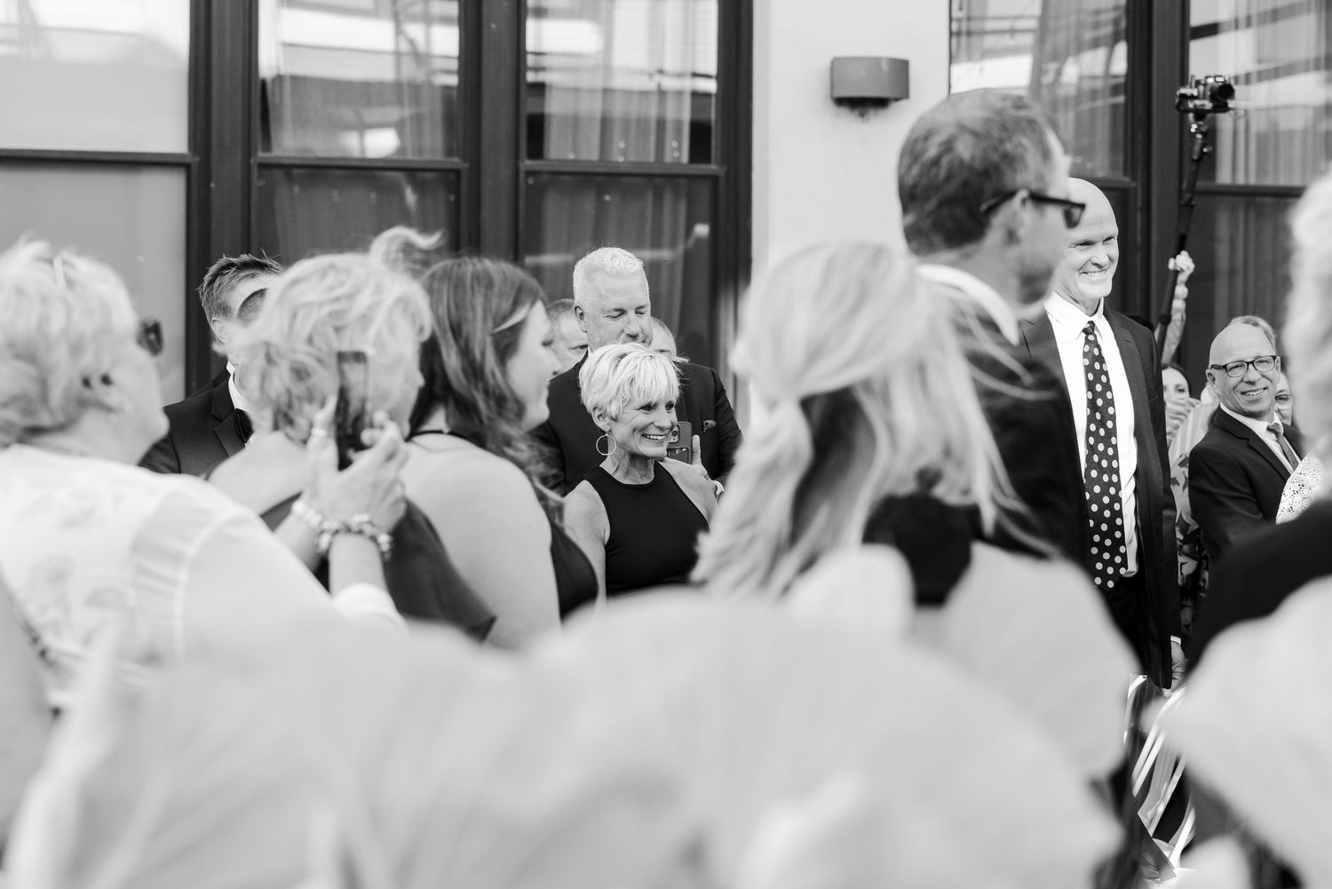 Black and white photo of wedding guests gathered indoors, smiling and celebrating at a elegant reception event.