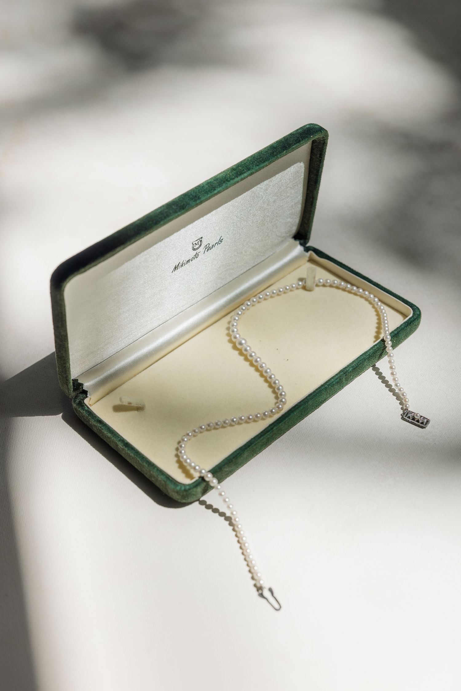 Elegant pearl necklace displayed in an open green jewelry box on a white surface with soft shadows.