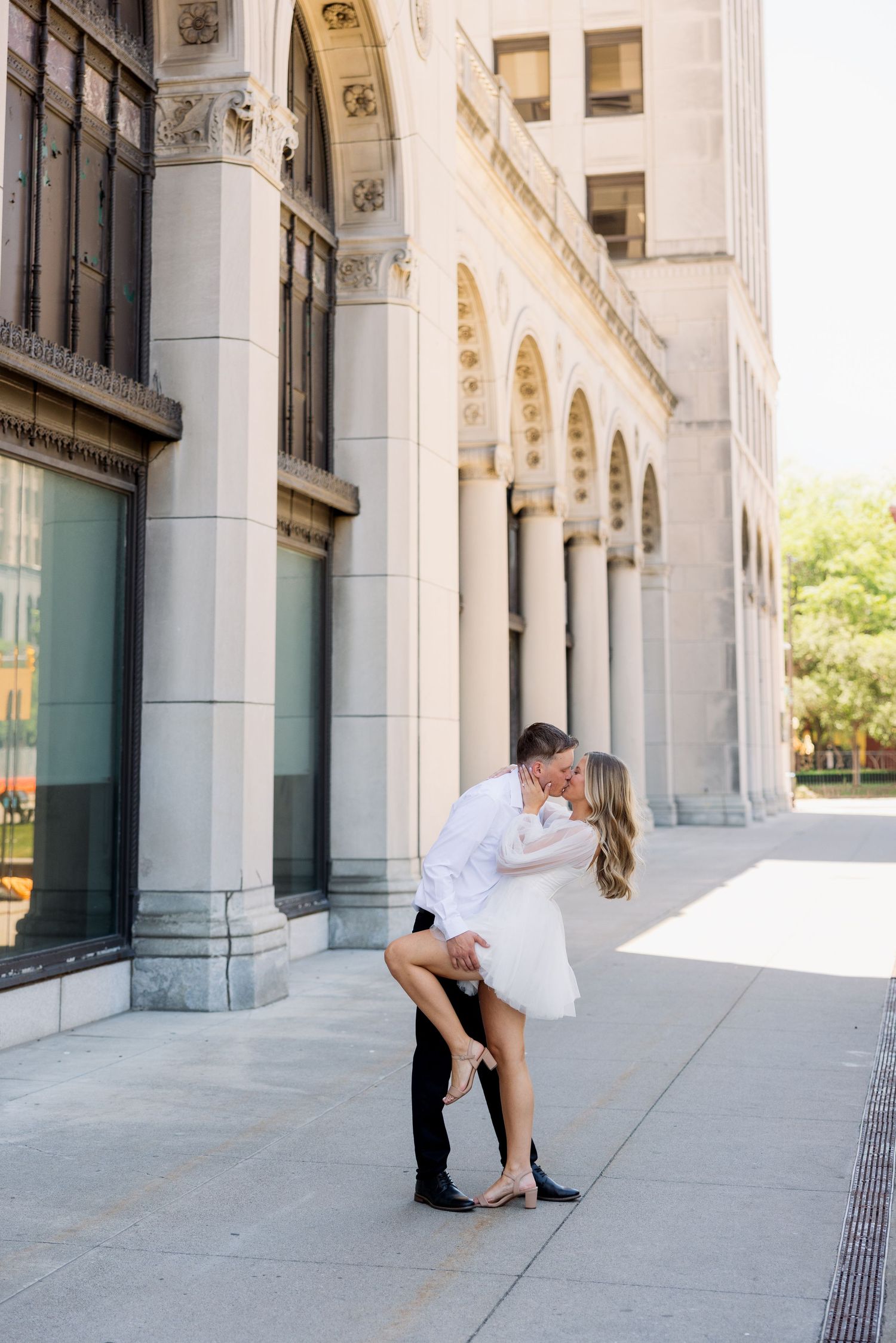 Couple sharing a romantic dip kiss in front of elegant white stone columns of a classic building.