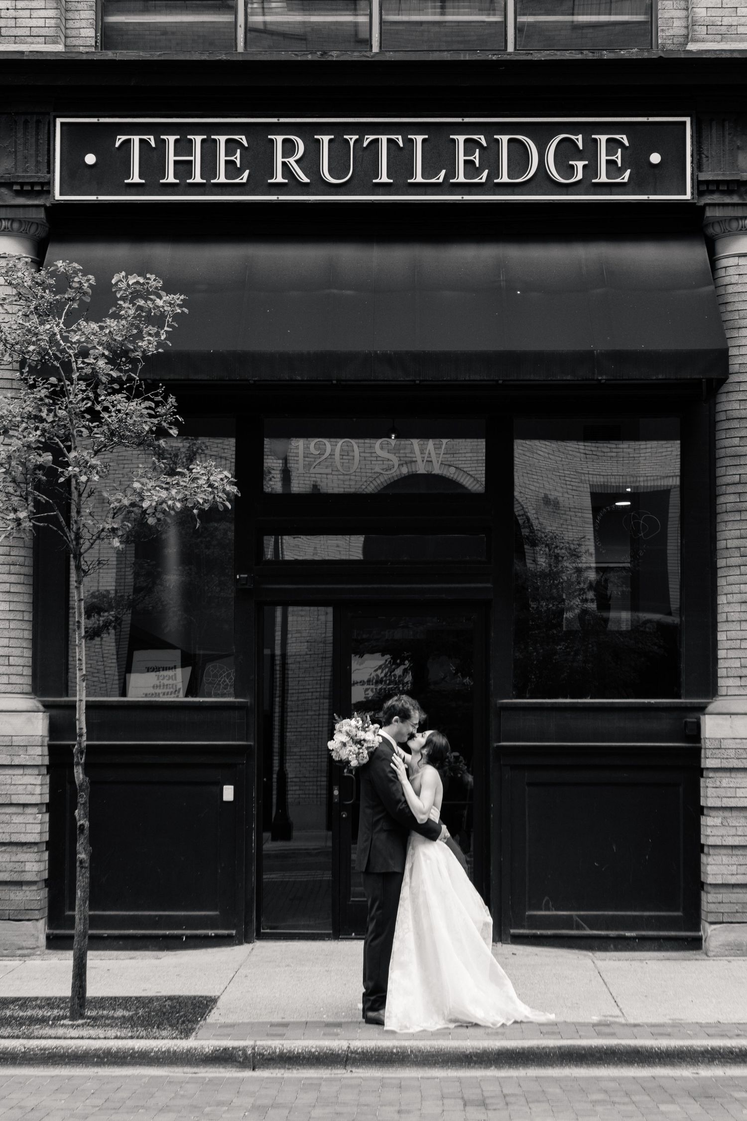 Bride and groom share a kiss outside The Rutledge building in a black and white wedding portrait.