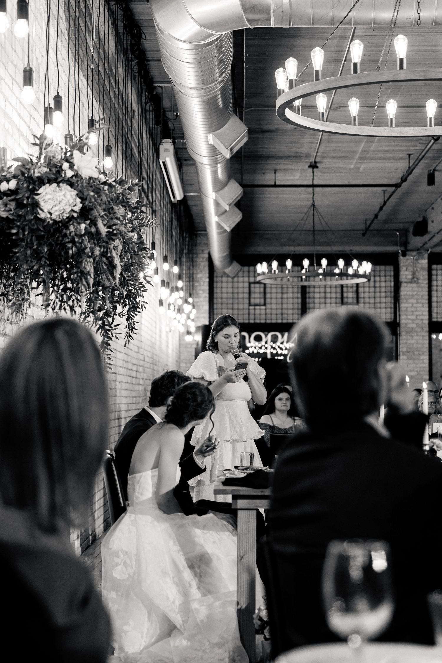 Bridesmaid giving a heartfelt speech at an elegant indoor wedding reception, black and white.