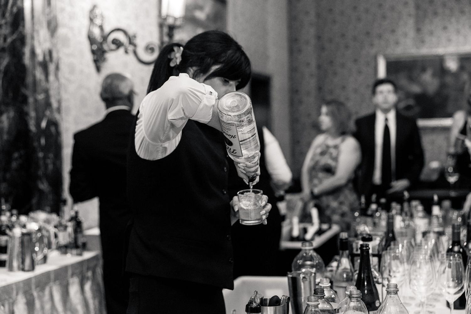 Bartender skillfully pouring drinks at a formal wedding reception bar in black and white.
