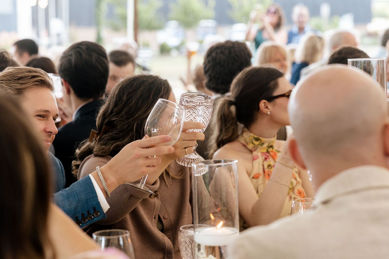 Wedding guests raising glasses in a toast at an elegant outdoor reception celebration.