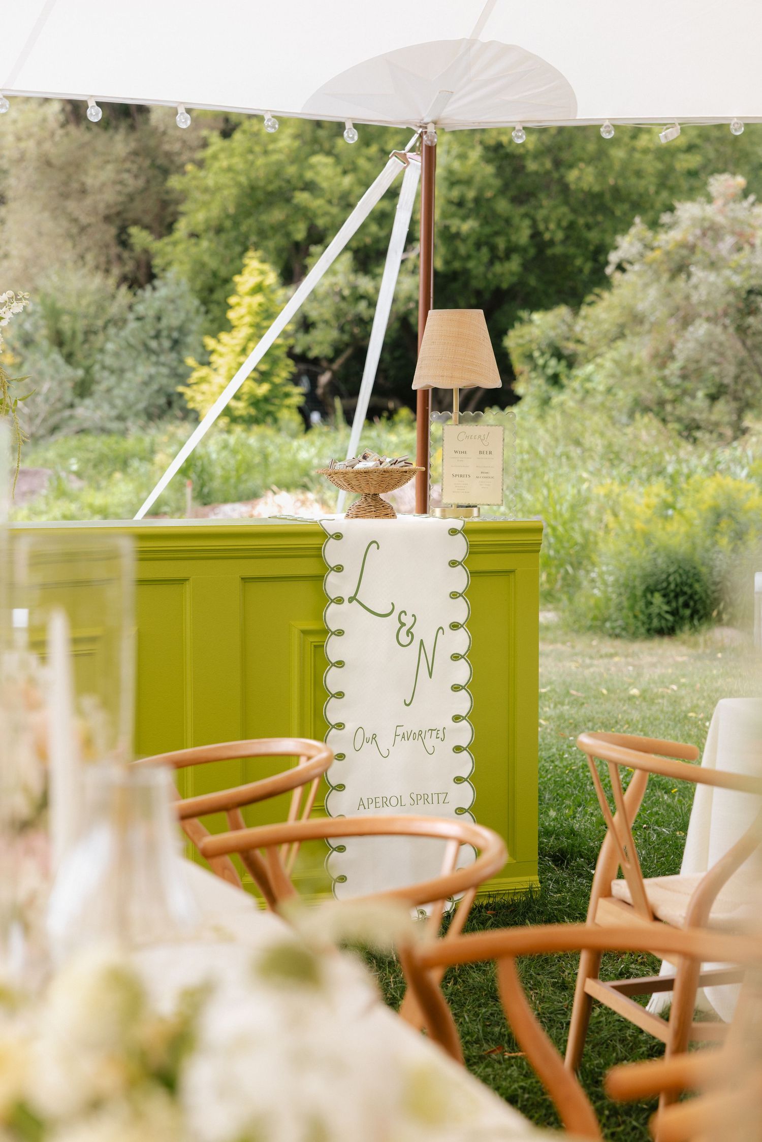 Chartreuse bar with L&N monogram sign and Aperol Spritz banner at an outdoor garden wedding reception.