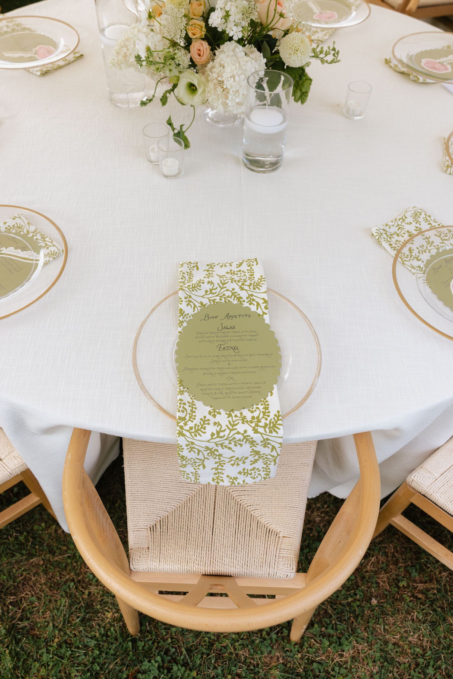 Elegant wedding reception table with white linen, gold-rimmed plates, floral centerpiece, and green botanical menu card.