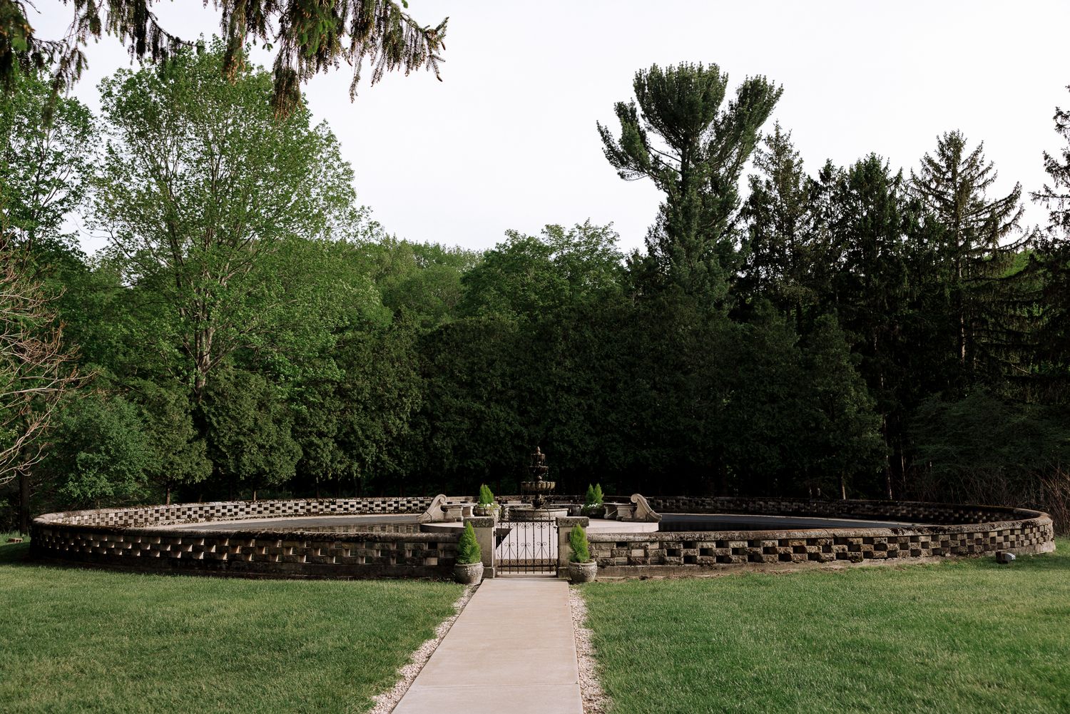 Stone garden wall with ornate gate surrounded by lush green trees on a grassy lawn.