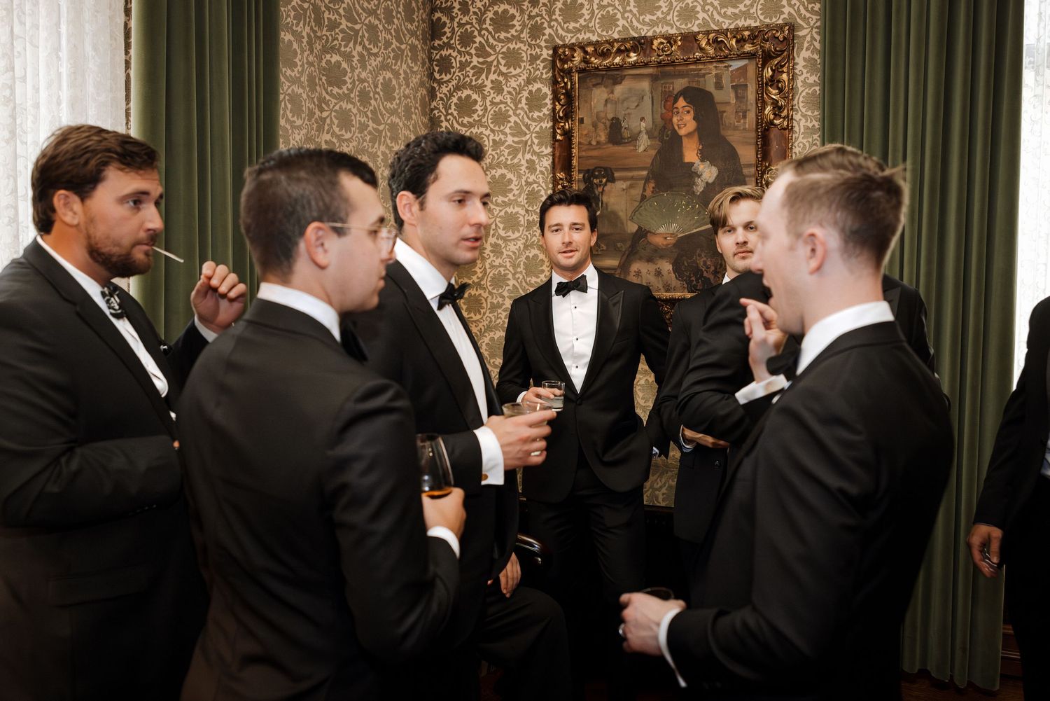 Groomsmen dressed in black tuxedos conversing at a sophisticated wedding reception venue.