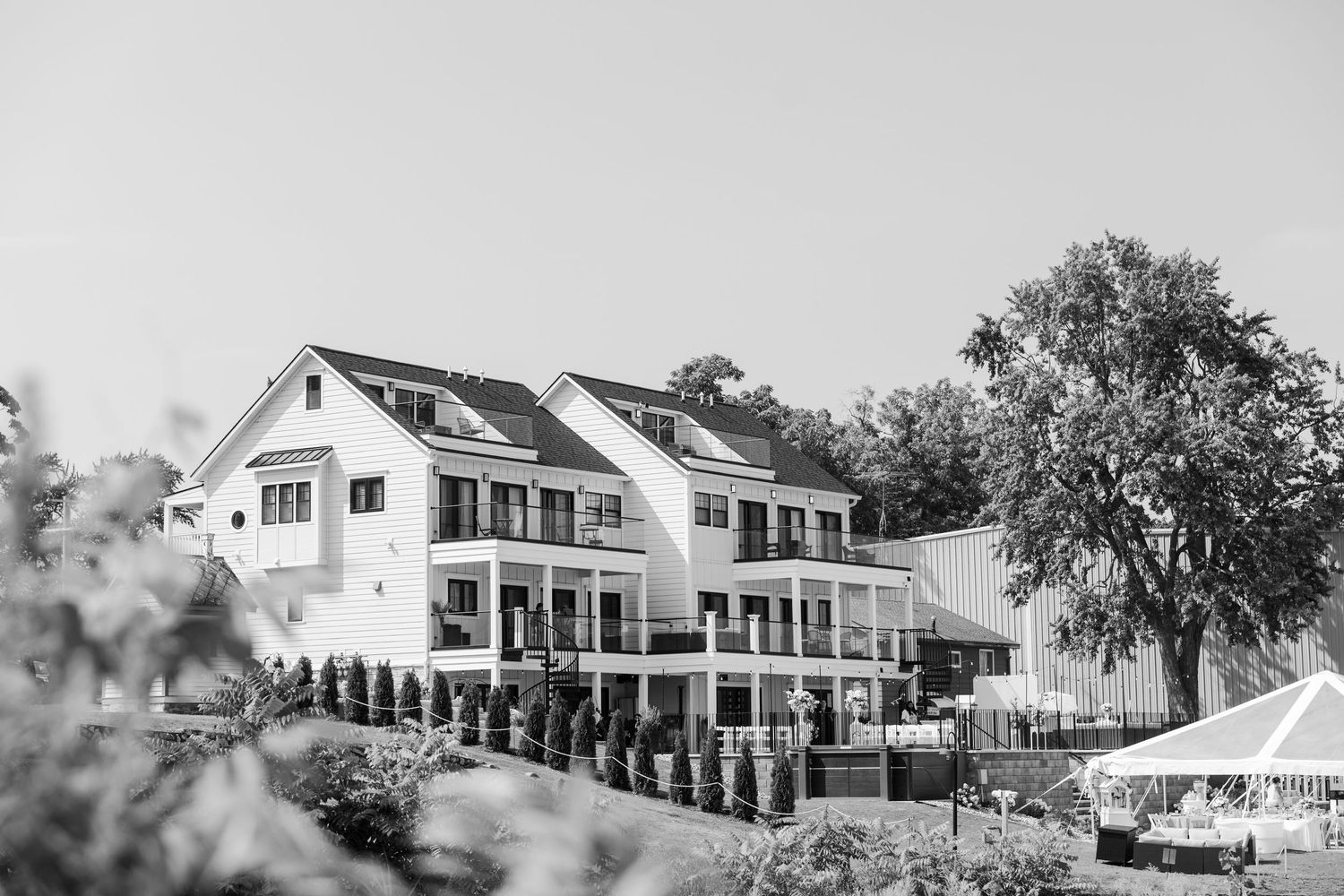 Black and white photo of a large white colonial inn with wraparound porches surrounded by trees and landscaping.