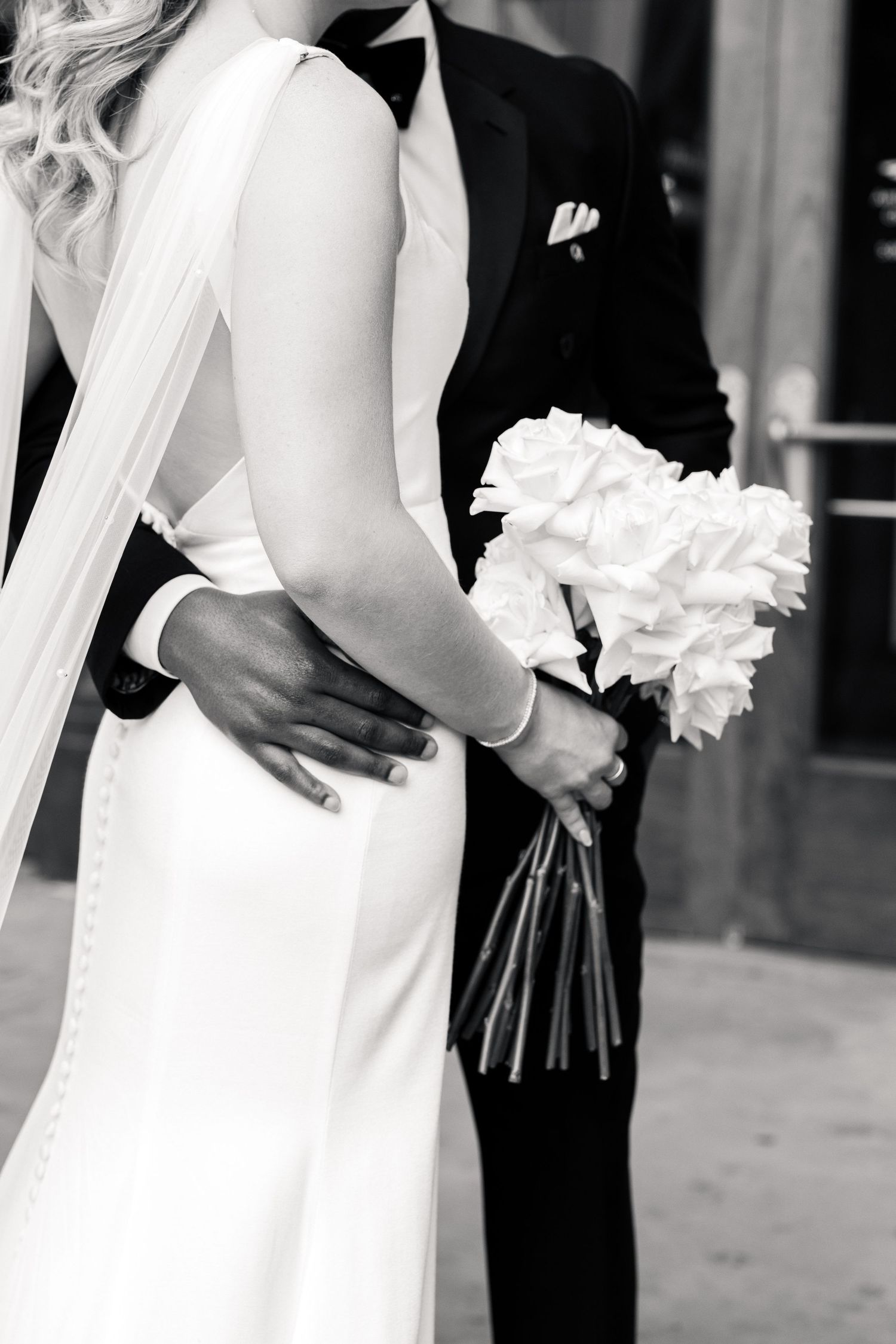 Classic black and white photo of bride in fitted white gown and groom in tuxedo sharing an embrace.