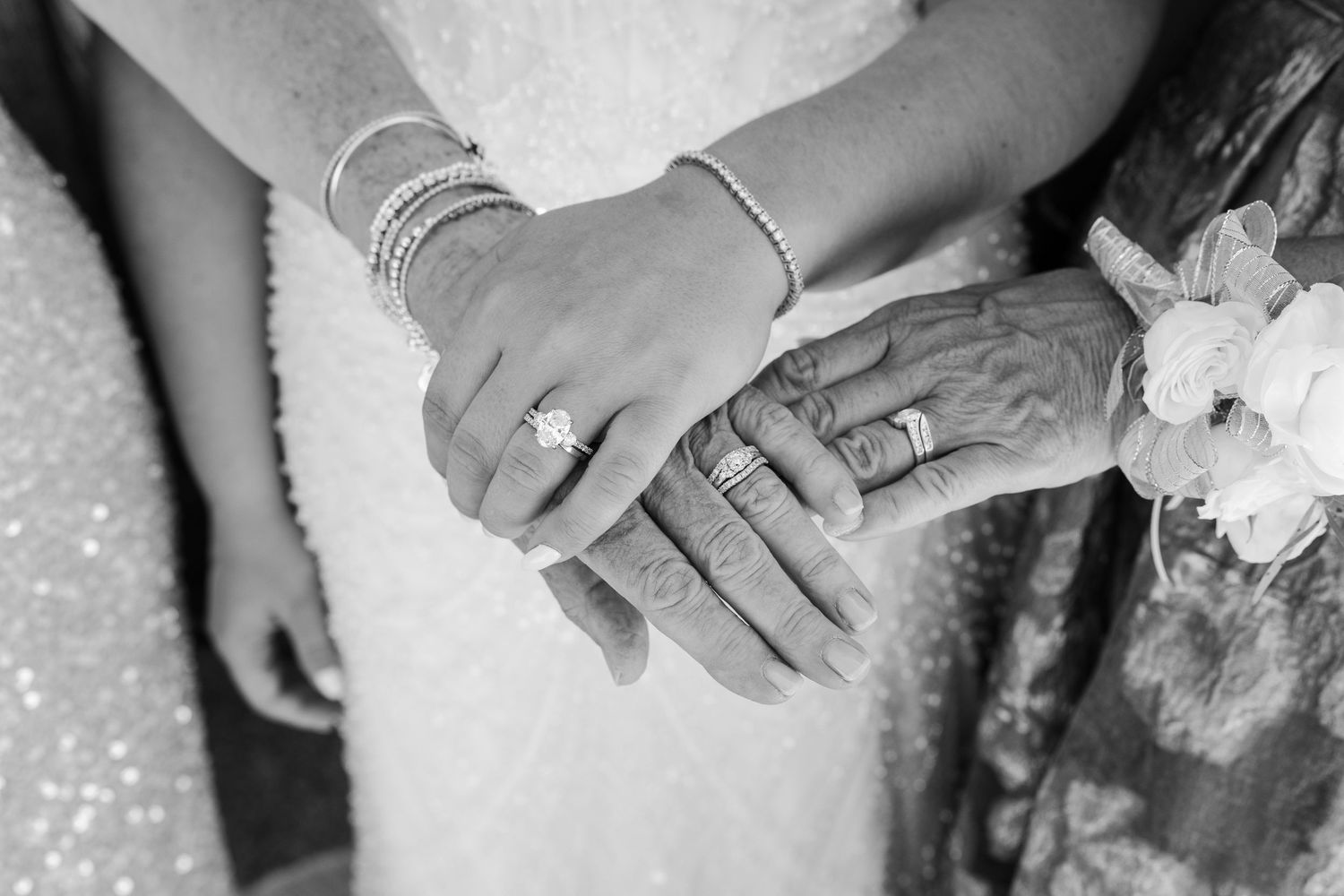 Close-up of bride and elderly woman's hands showing wedding rings and bracelets at a wedding ceremony.