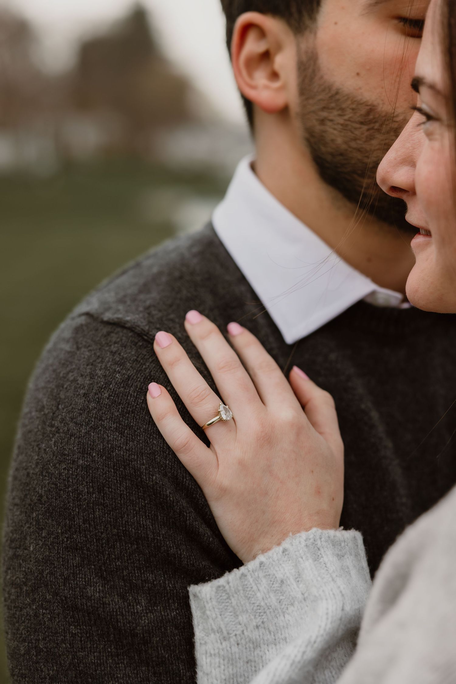 Close-up of a woman's hand with an engagement ring resting on her partner's gray sweater.