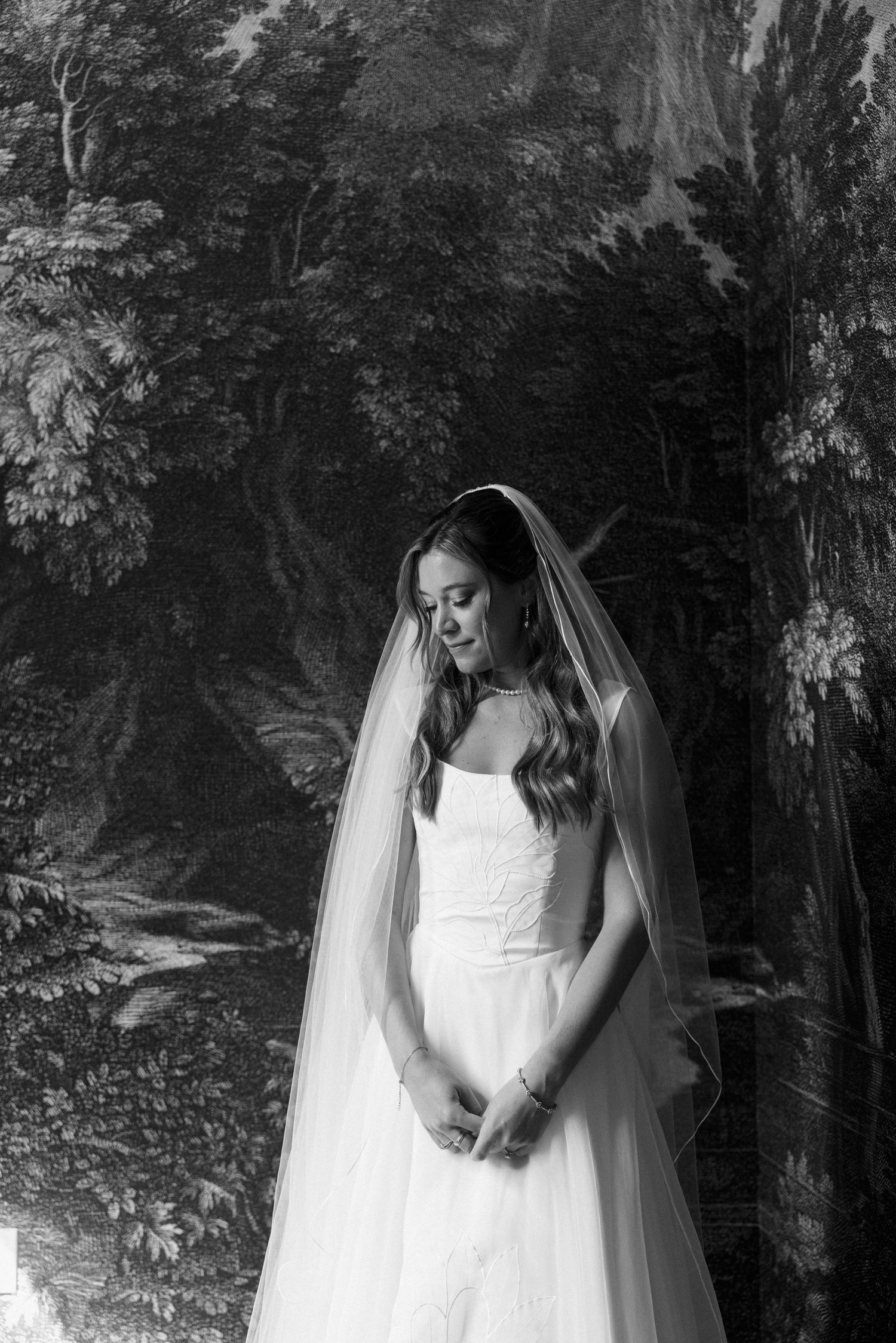 Black and white bridal portrait of a bride in a wedding gown and veil, posing gracefully before a scenic backdrop.