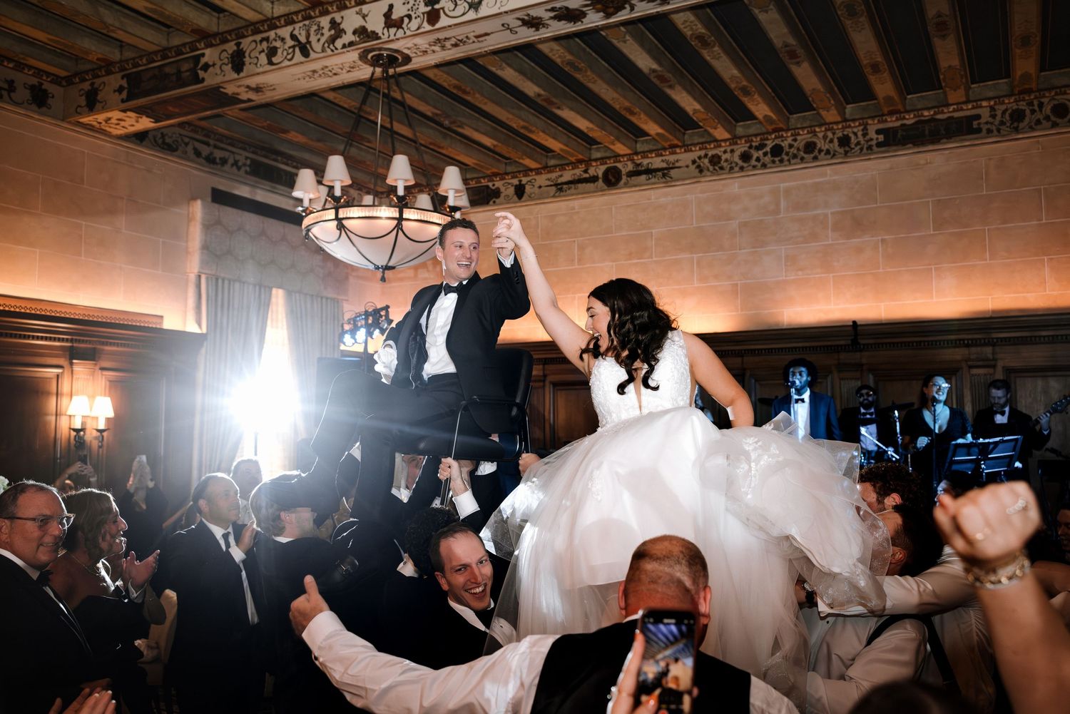 Bride and groom waving napkins while lifted high during celebratory hora dance.