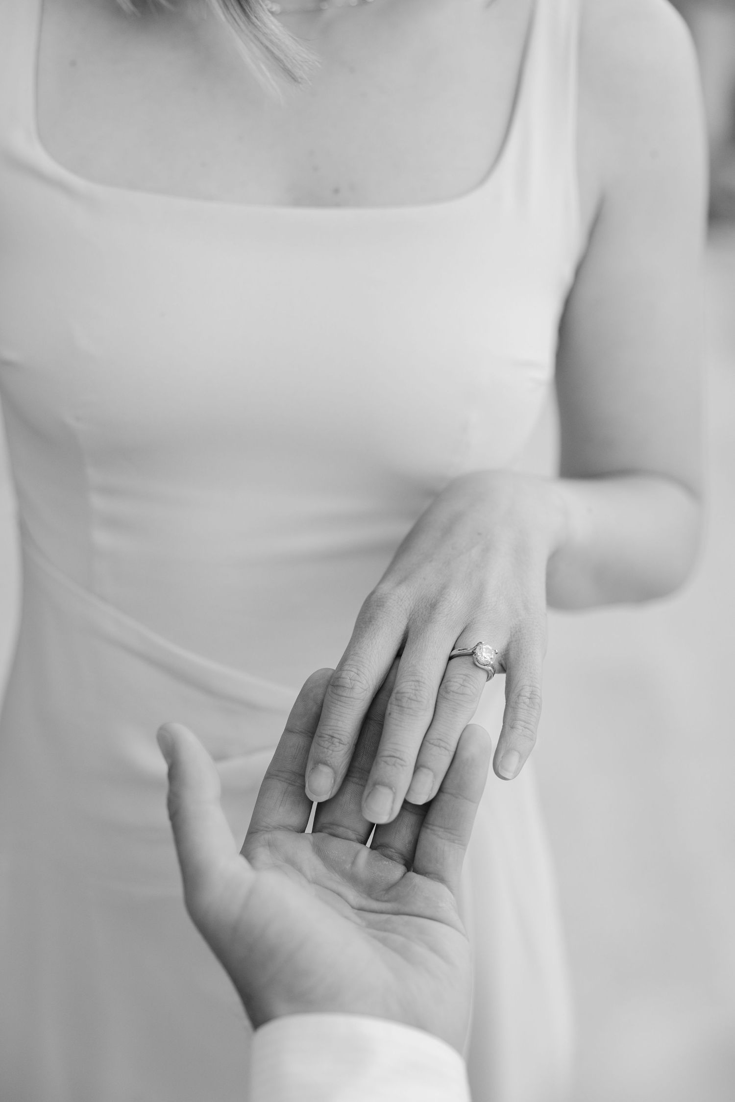 Black and white photo of a bride wearing an engagement ring placing her hand in her groom's hand.