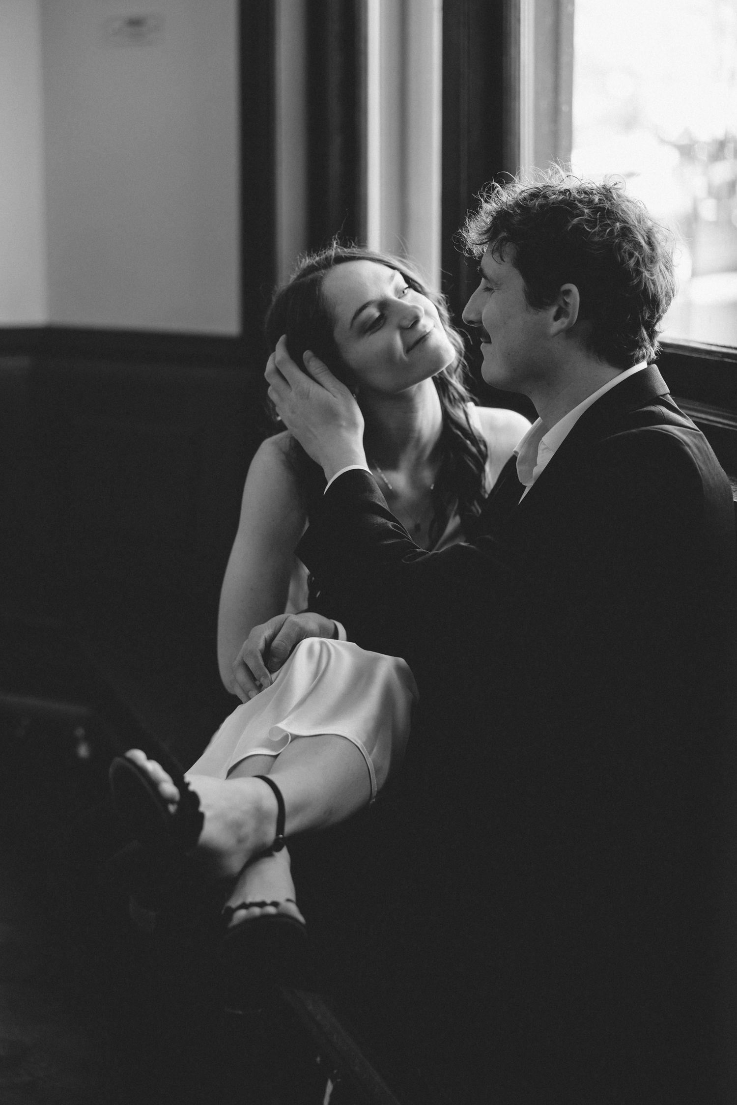 Black and white photo of couple sharing tender moment by window indoors.
