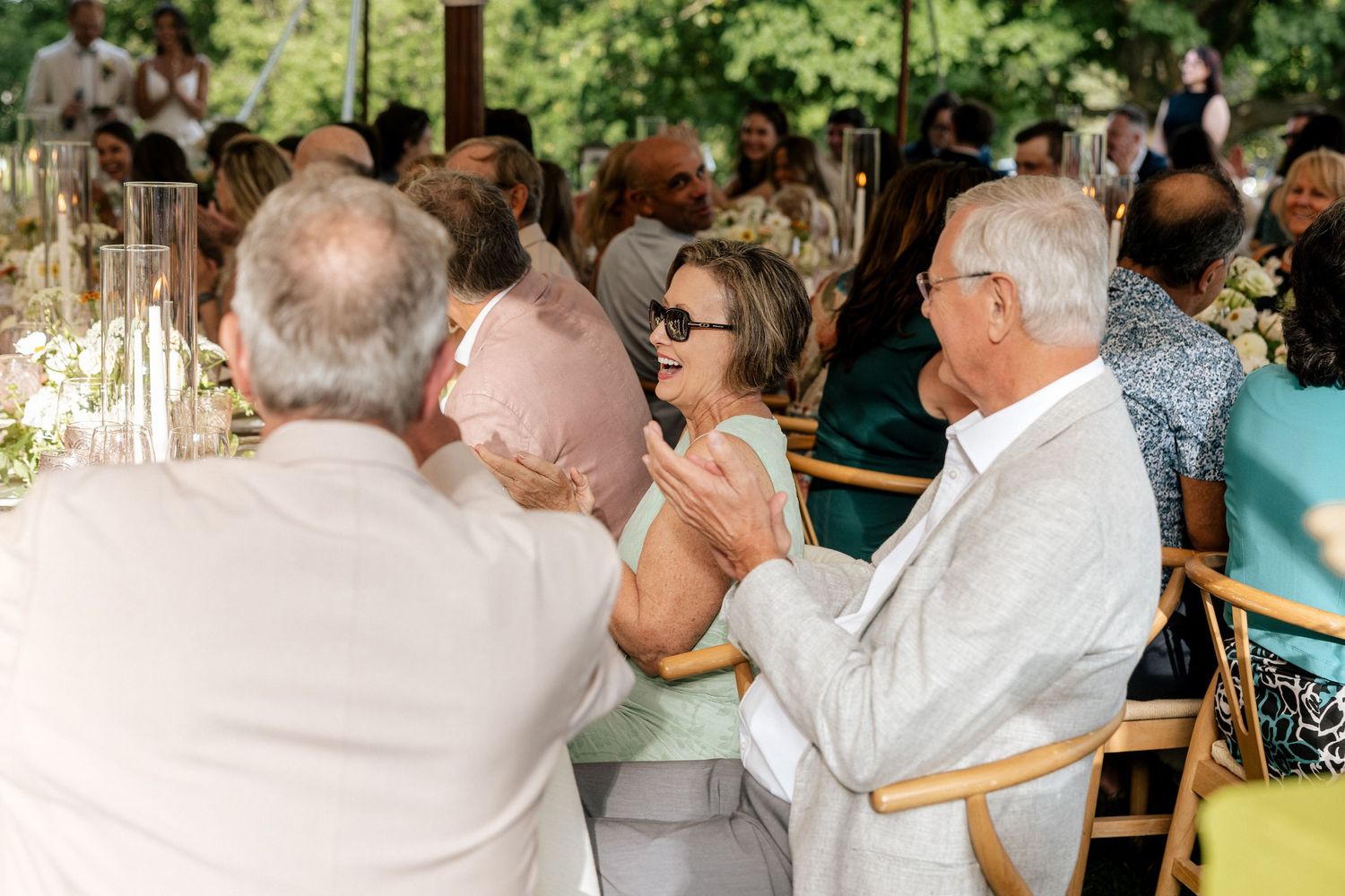 Elegantly dressed wedding guests socializing and clapping at an outdoor garden wedding reception.