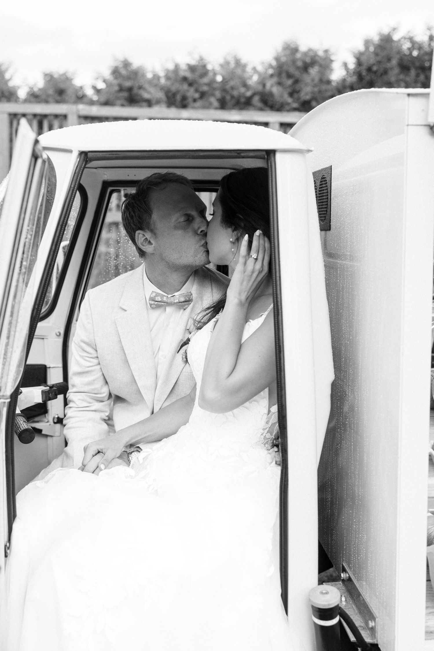 Black and white photo of bride and groom sharing a kiss inside a vintage white van.