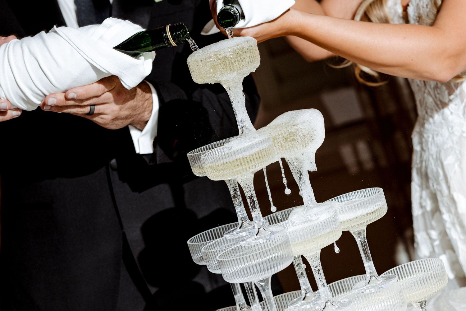 Champagne tower being filled at a wedding reception with sparkling wine cascading down crystal coupe glasses.