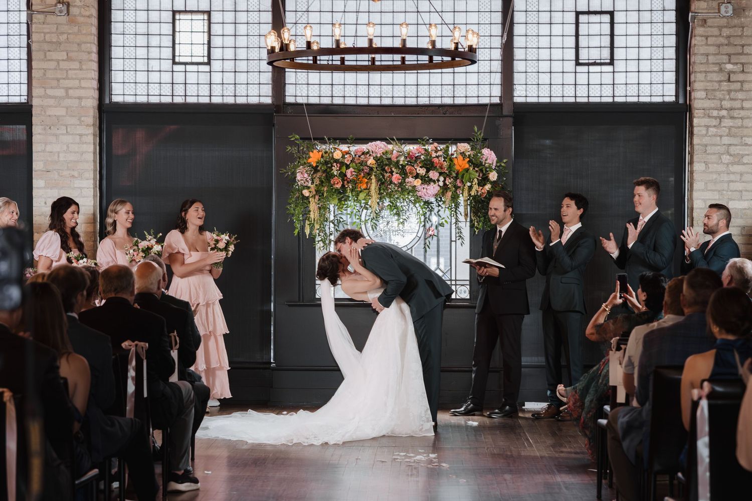 Groom dips bride at altar during wedding ceremony as guests and bridal party applaud.