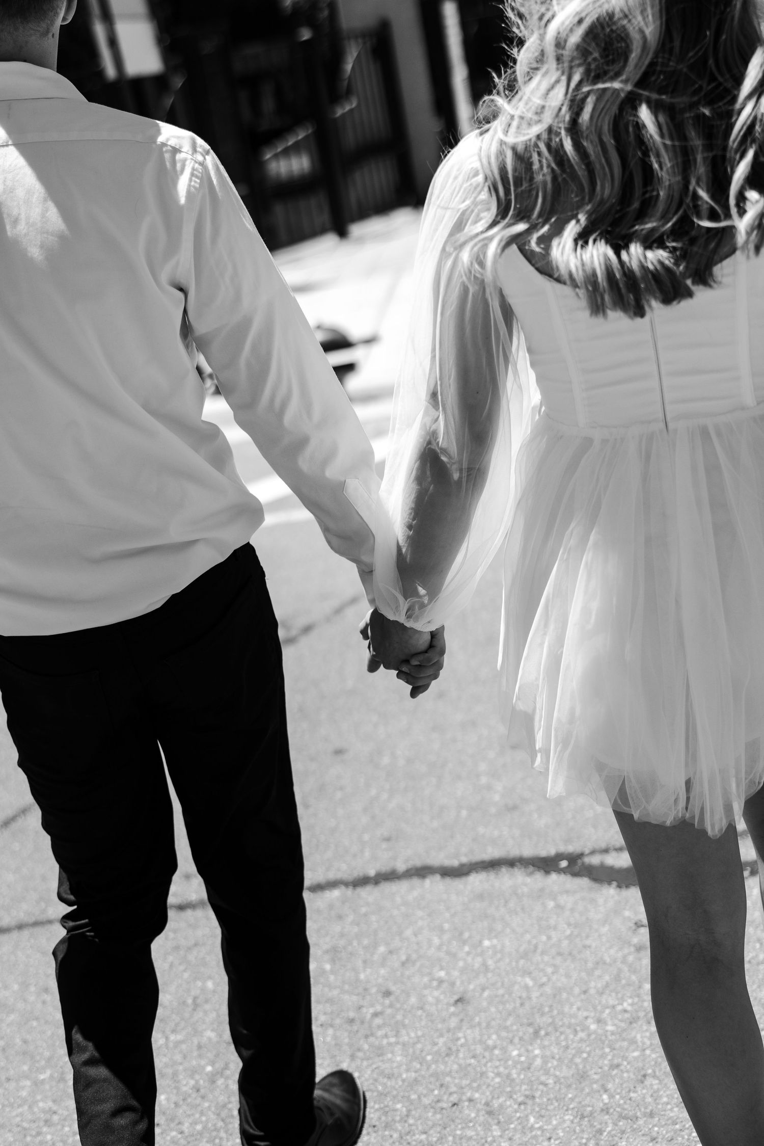Black and white photo of a couple holding hands while walking, woman in white dress and man in dark pants.