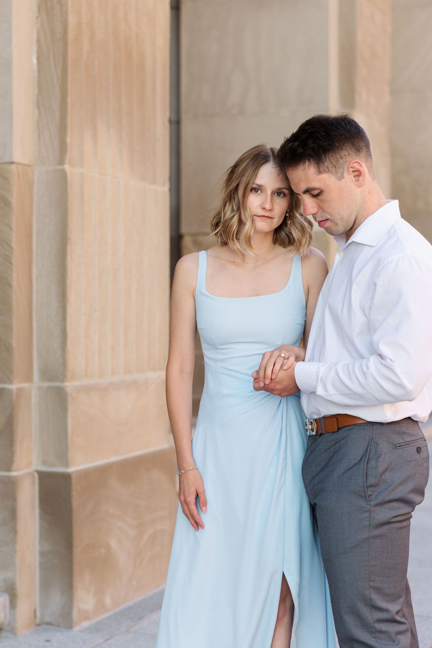 Couple in light blue dress and white shirt tenderly hold hands against a stone wall.