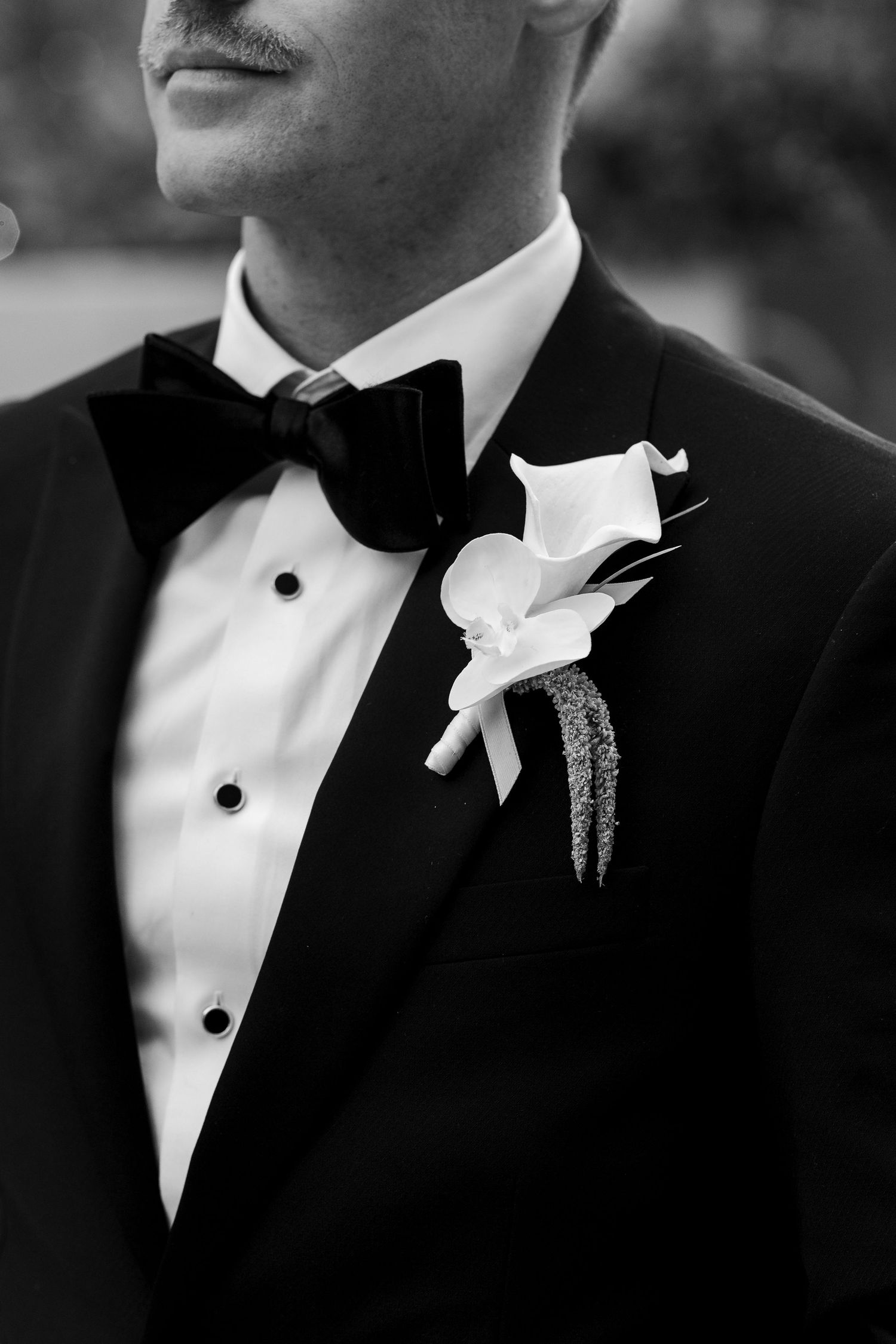 Black and white photo of groom in tuxedo with bow tie and calla lily boutonniere on wedding day.