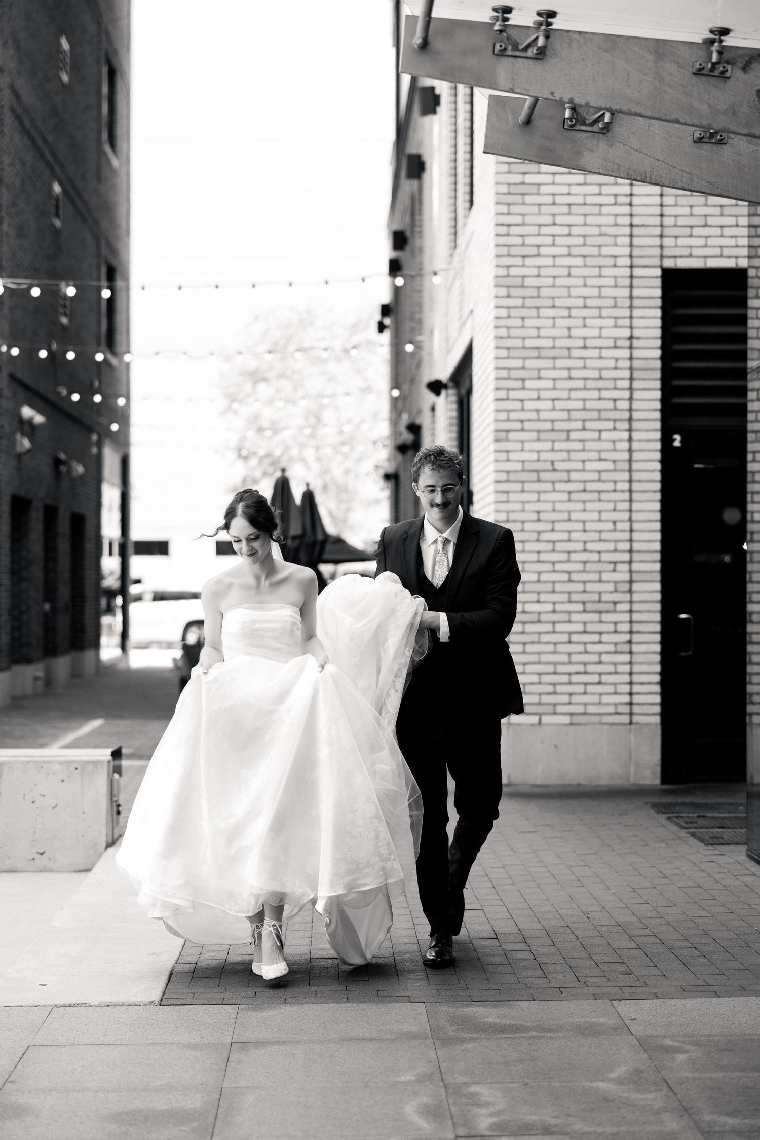 Black and white photo of bride and groom walking together along a city sidewalk.