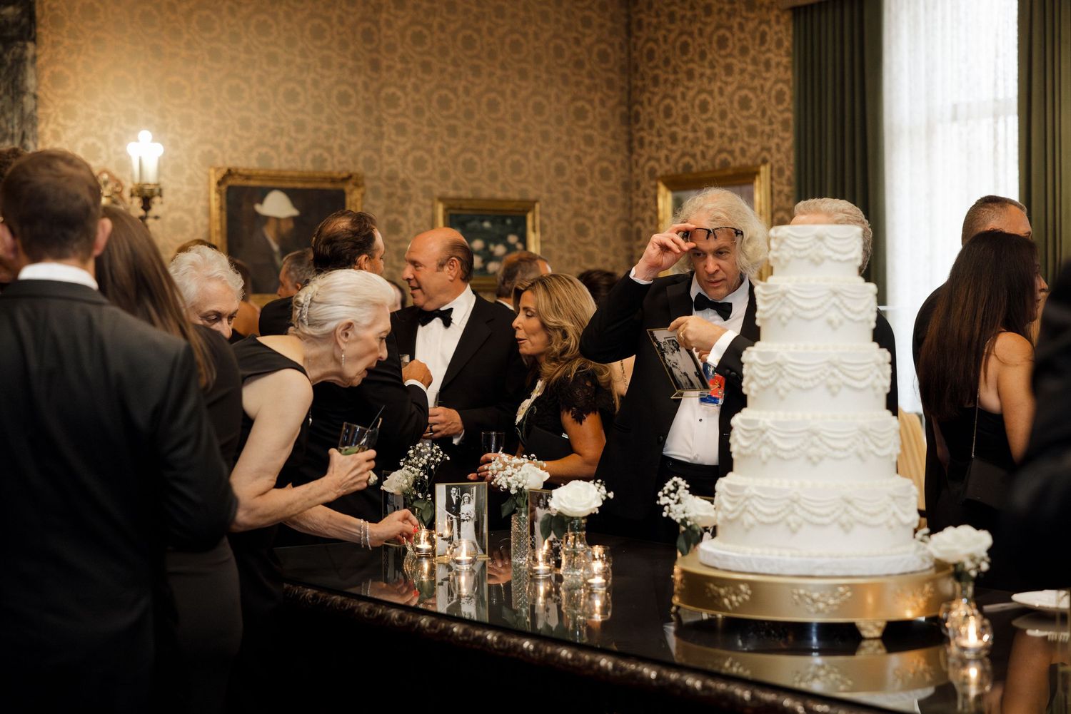 Wedding guests in formal attire gathered around a stunning multi-tiered white wedding cake.