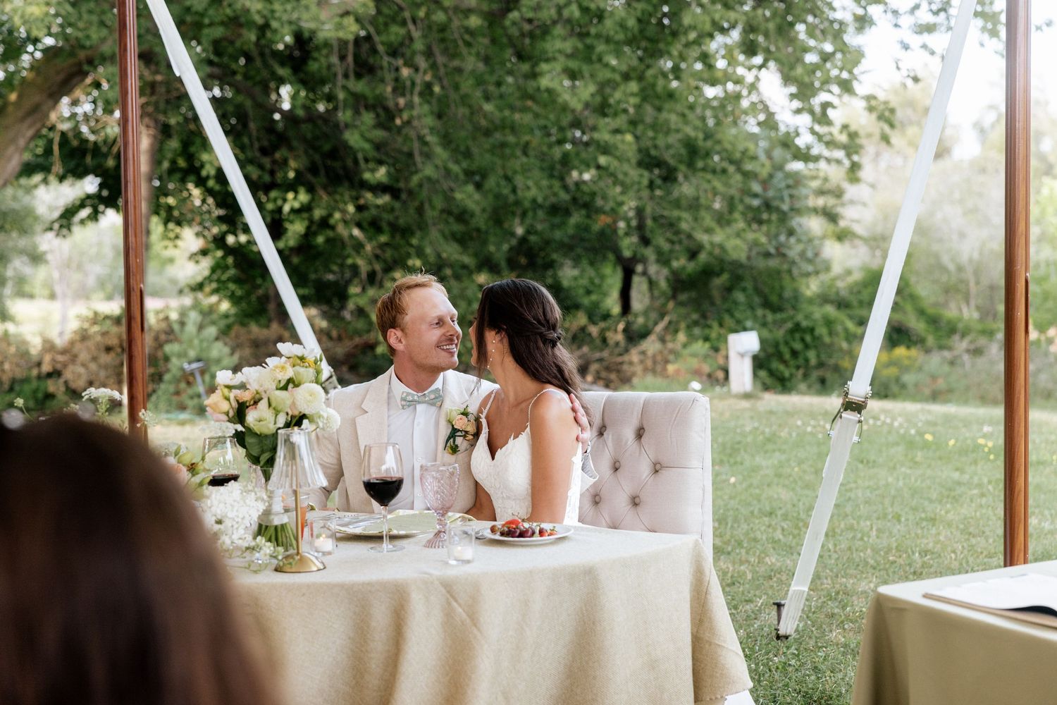 Bride and groom share a romantic moment at their sweetheart table during an elegant outdoor wedding reception.