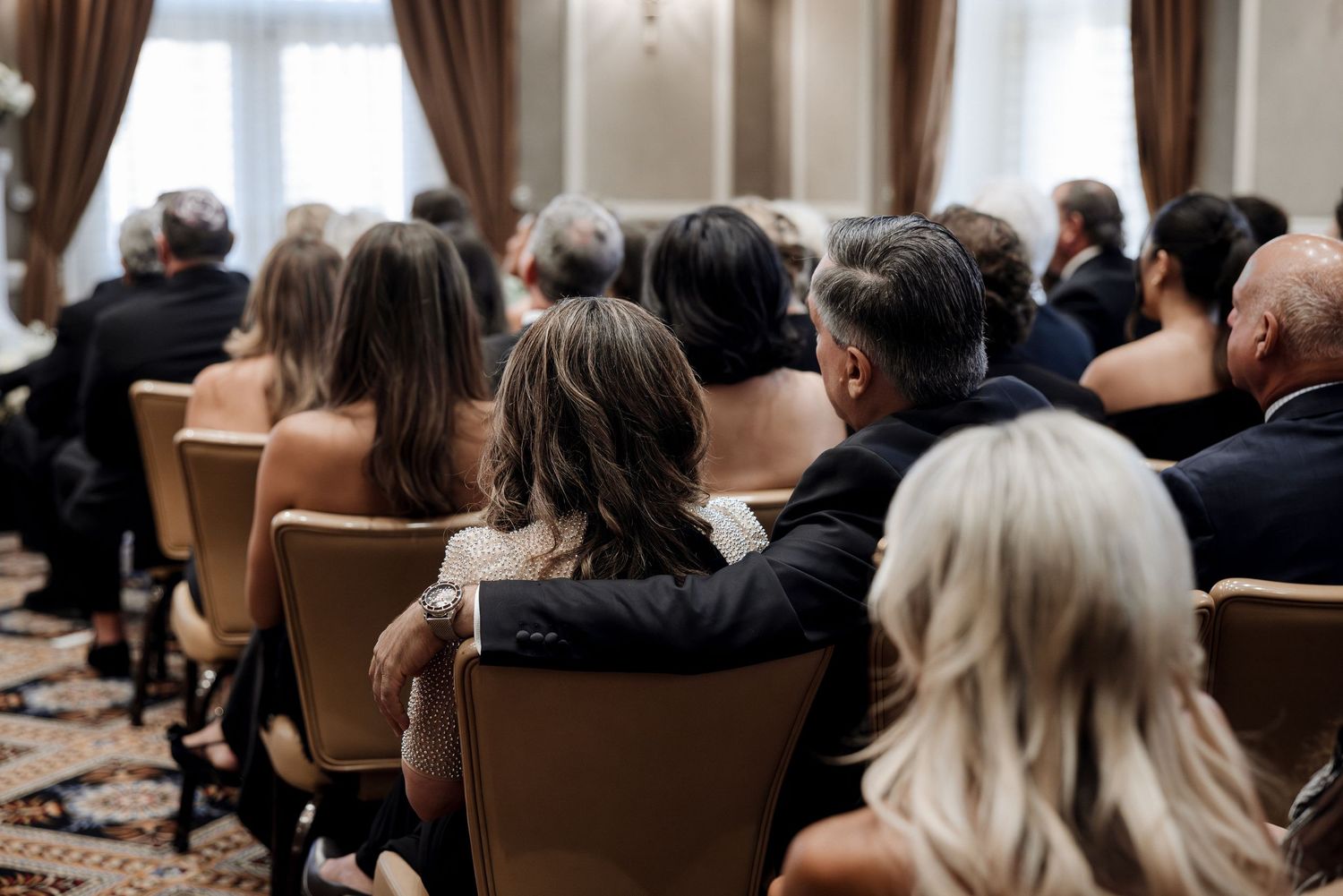 Wedding guests seated in gold chairs watch the ceremony, with a couple sharing an intimate embrace.