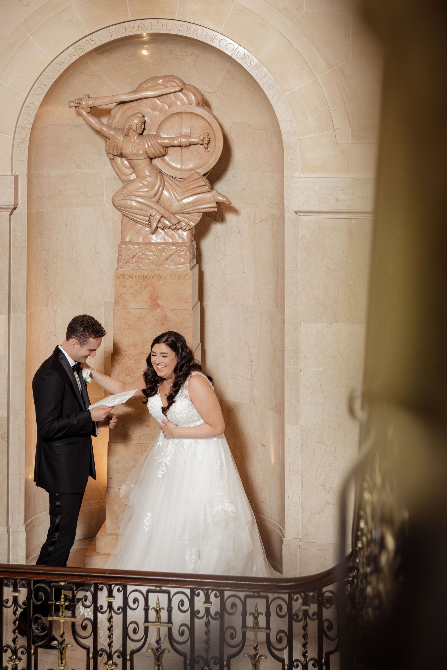 Bride and groom exchange vows on ornate staircase with marble relief.