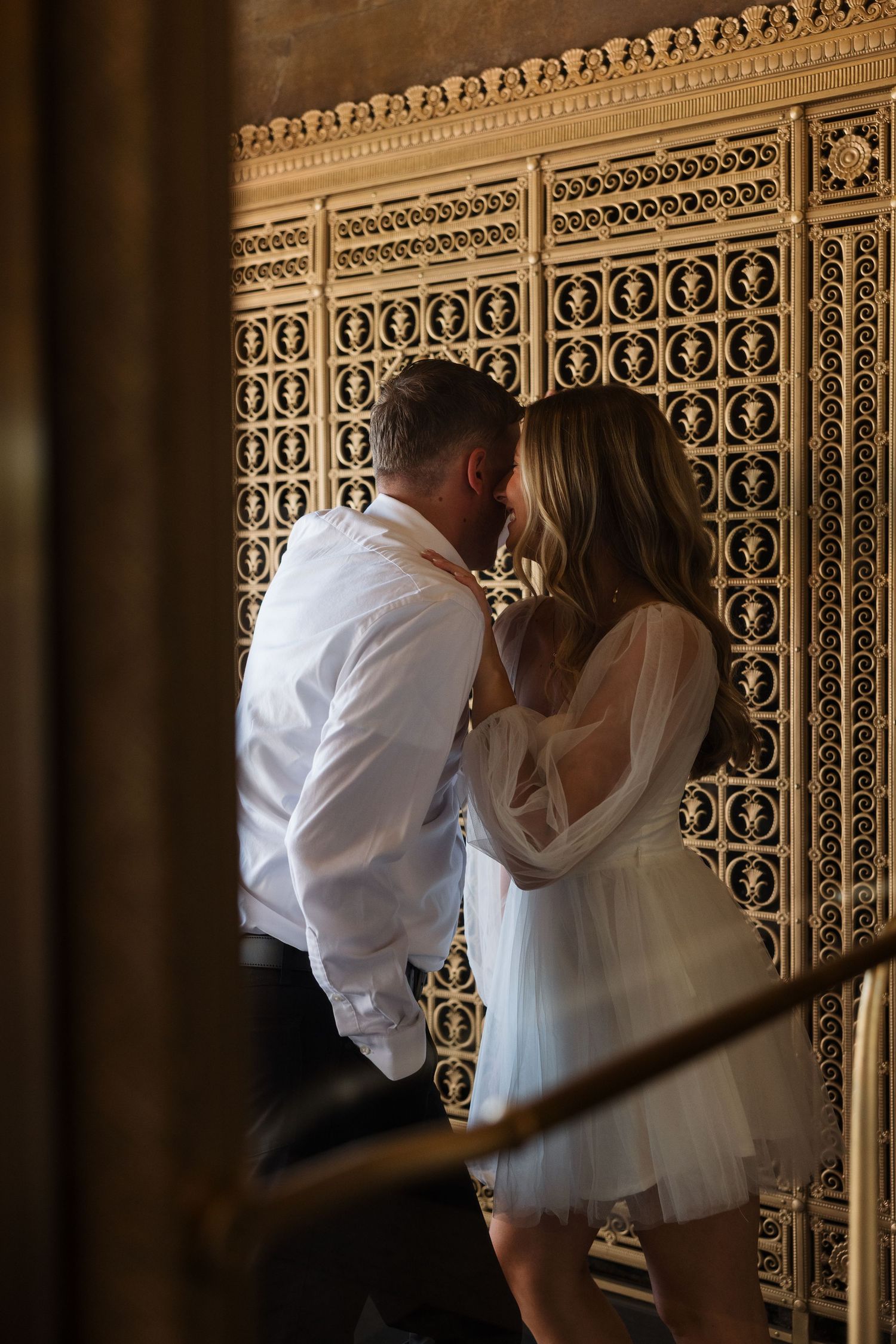 Couple sharing a romantic moment in front of ornate golden decorative wall panel in elegant venue.