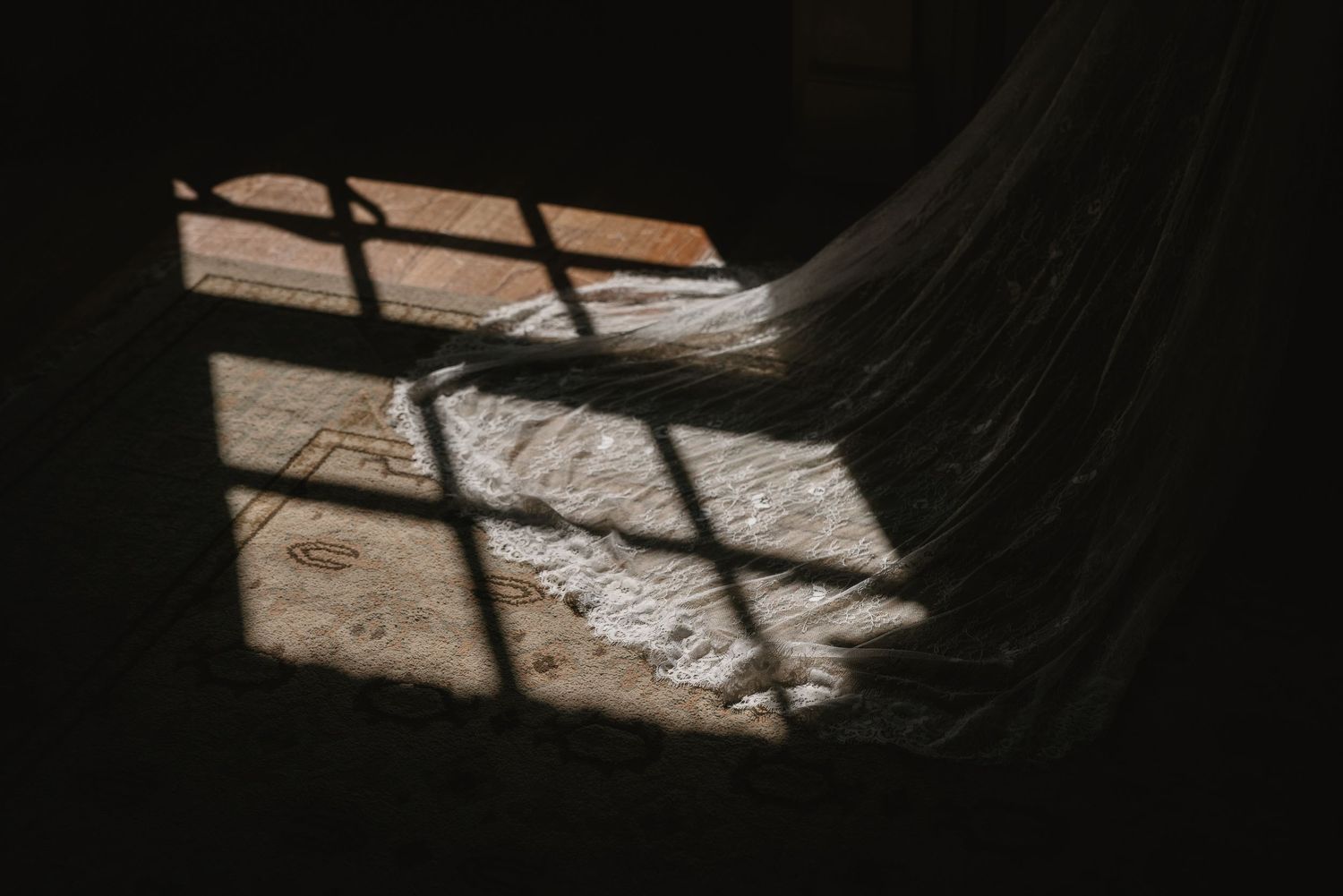 Sunlight casting diamond grid shadows through a window onto a rustic floor with sheer fabric draped nearby.