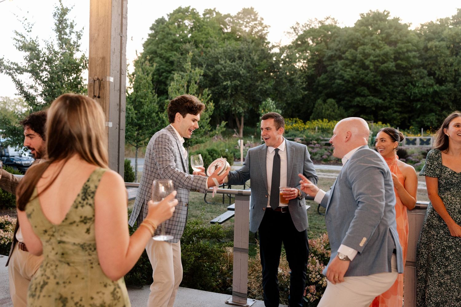 Elegantly dressed guests mingling and toasting at an outdoor wedding reception on a terrace at dusk.