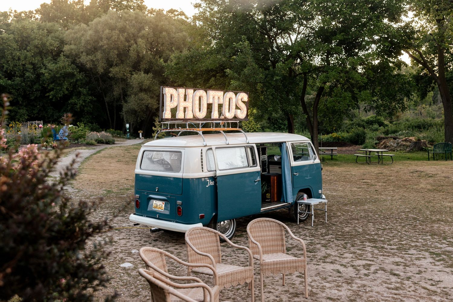 Vintage teal VW bus photo booth with illuminated PHOTOS sign at outdoor wedding venue.