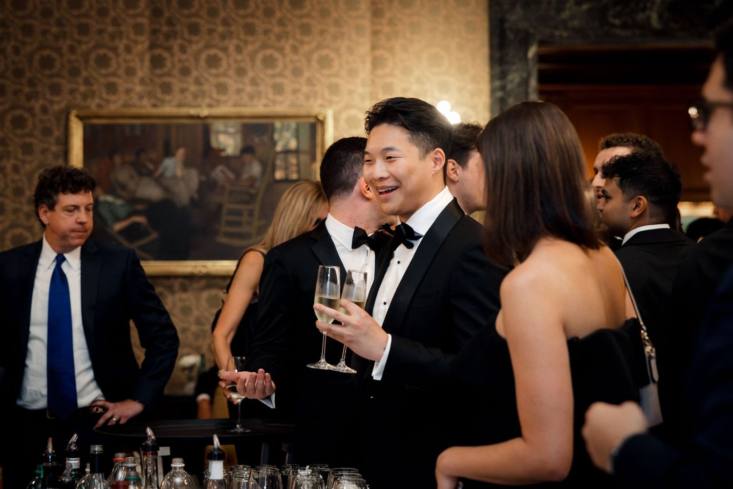 Couple in formal wear sharing a romantic moment while holding champagne at a wedding reception.