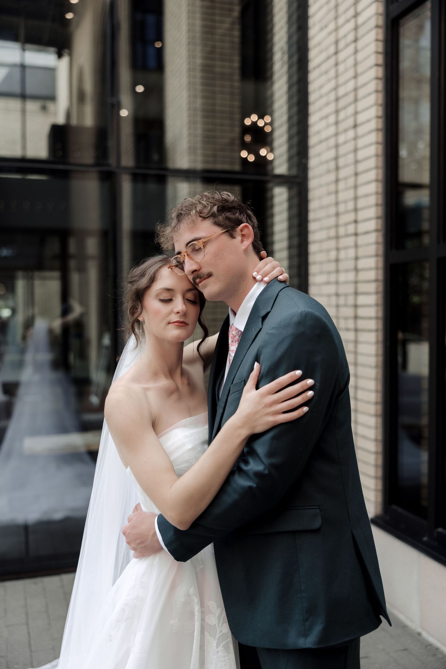Bride and groom in an intimate embrace outside a modern building with warm bokeh lights in the background.