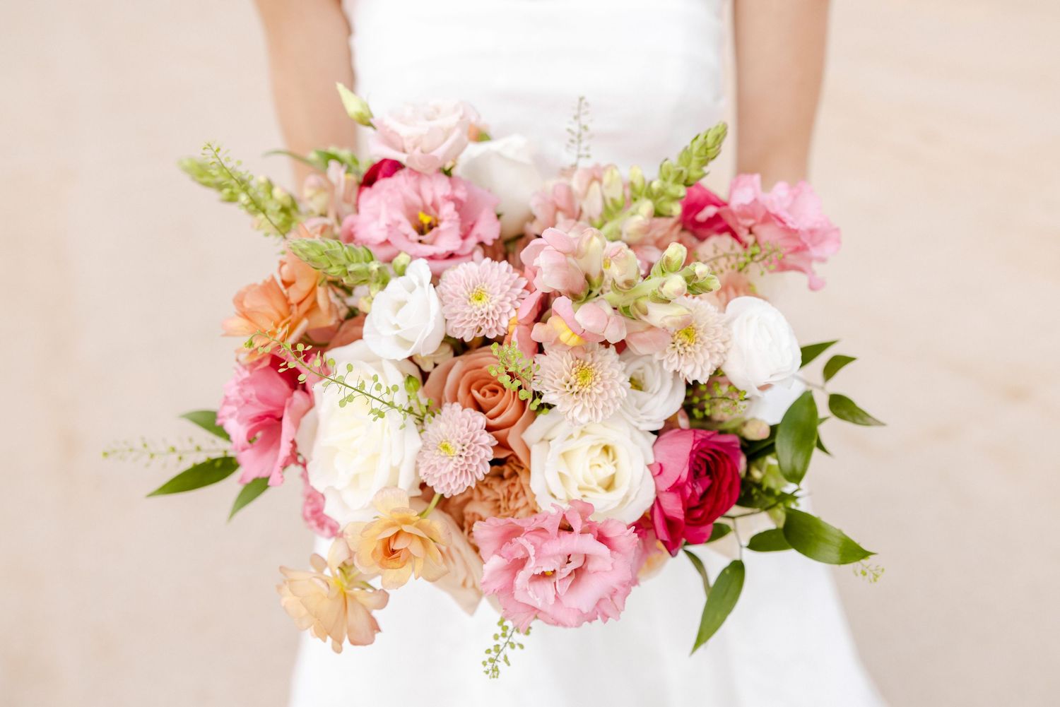 Bride holding a lush bridal bouquet of pink, peach, and white flowers including peonies and ranunculus.