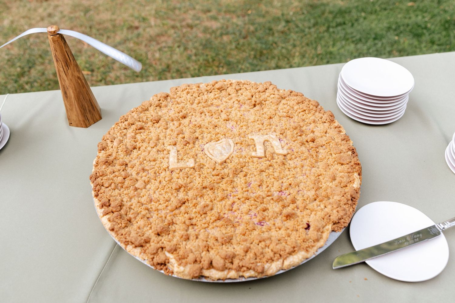Wedding pie with L and N initials in crumble topping displayed on table at outdoor reception.