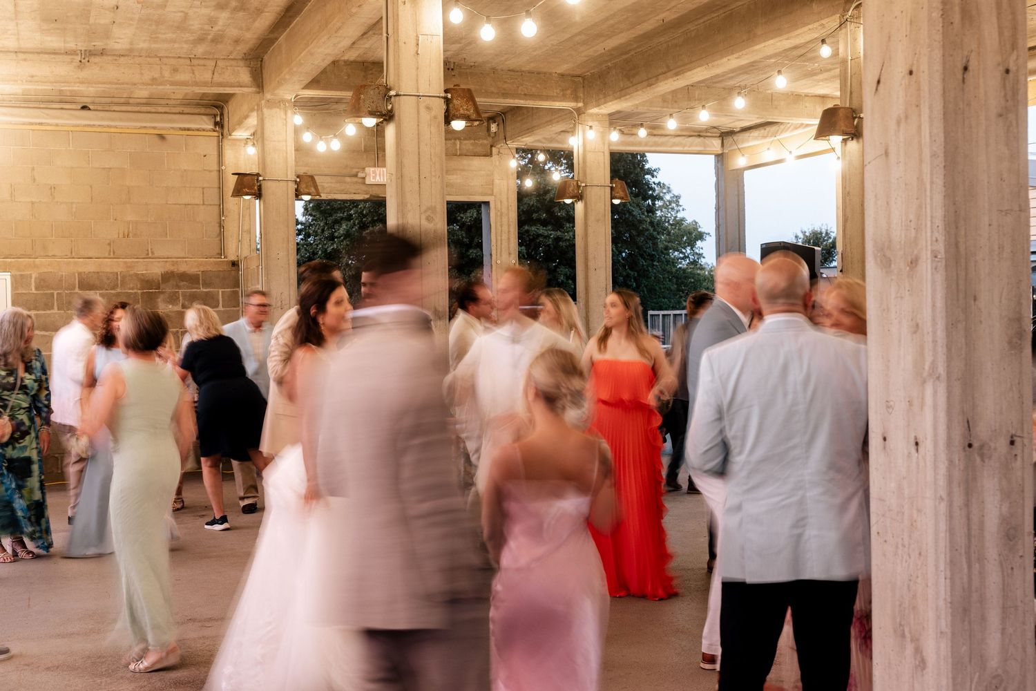 Guests dancing at an elegant outdoor wedding reception with string lights and rustic wooden columns.