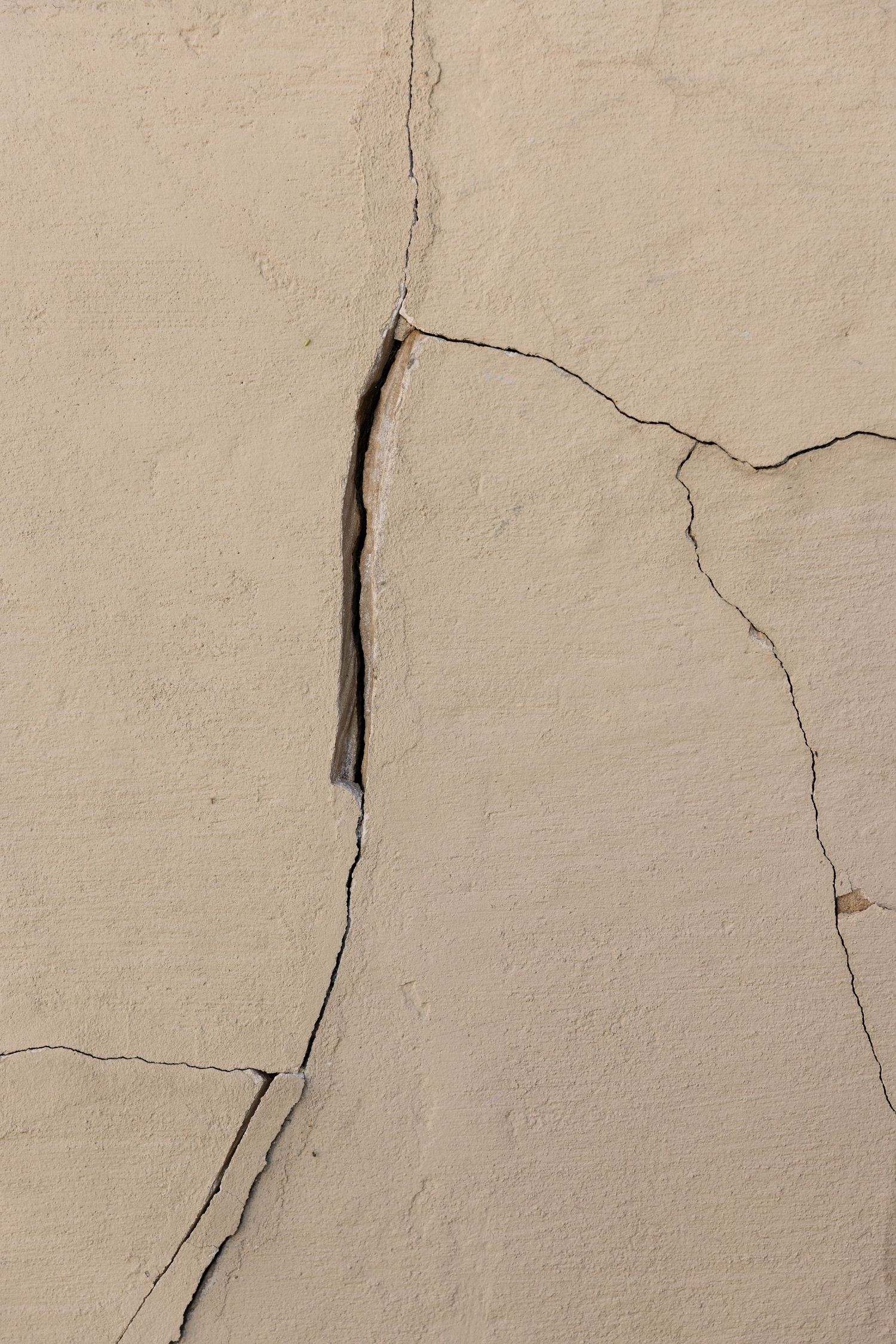 Close-up of a cracked beige concrete wall with multiple fractures and a visible gap in the surface.
