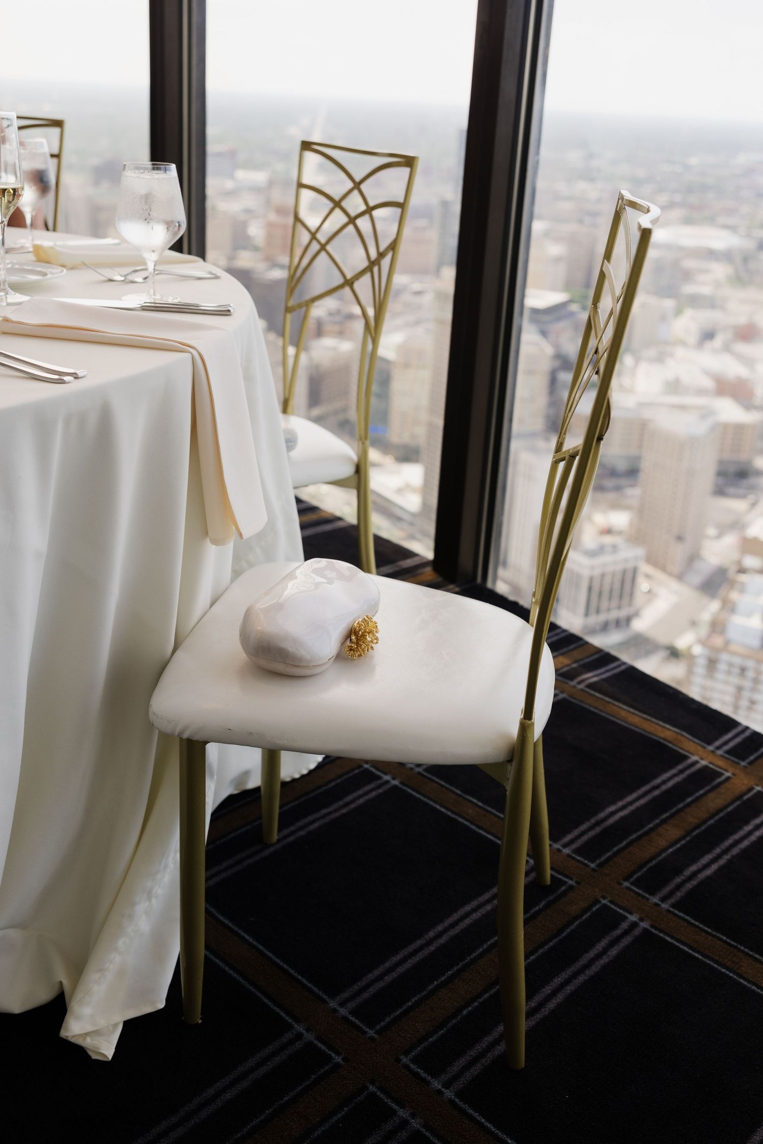 Elegant gold chiavari chair with white cushion at a high-rise restaurant table overlooking a city skyline.