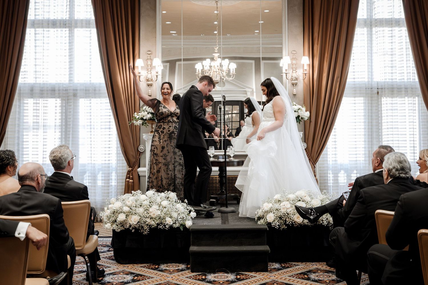 Bride and groom exchange vows at altar with white floral arrangements in a luxurious hotel ballroom ceremony.