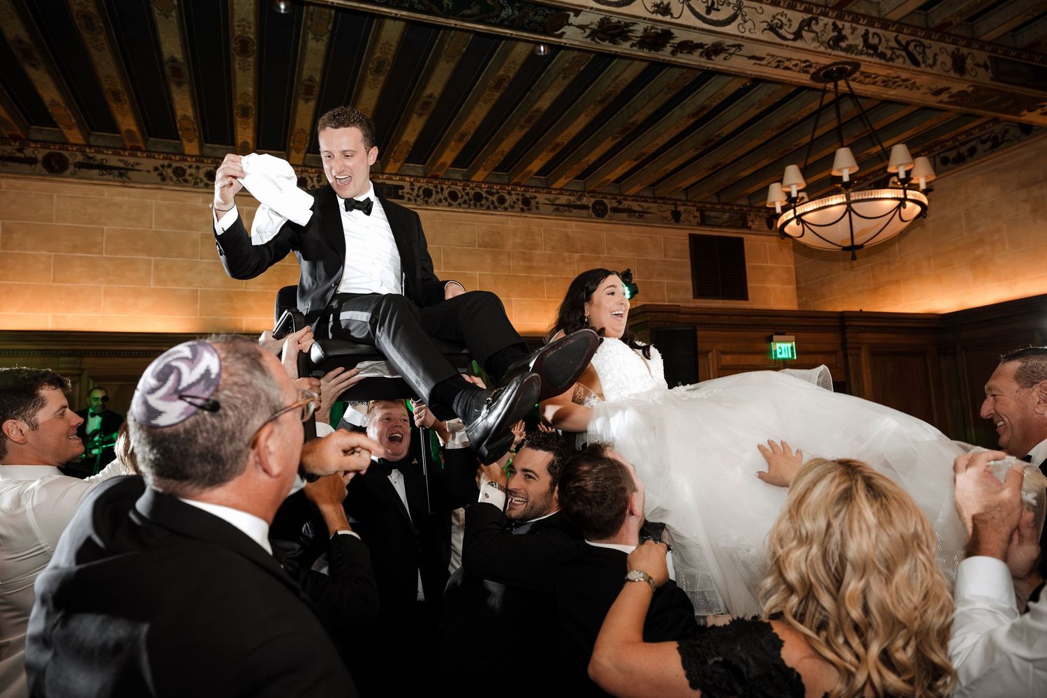 Bride and groom lifted by guests during traditional Jewish hora dance at wedding.