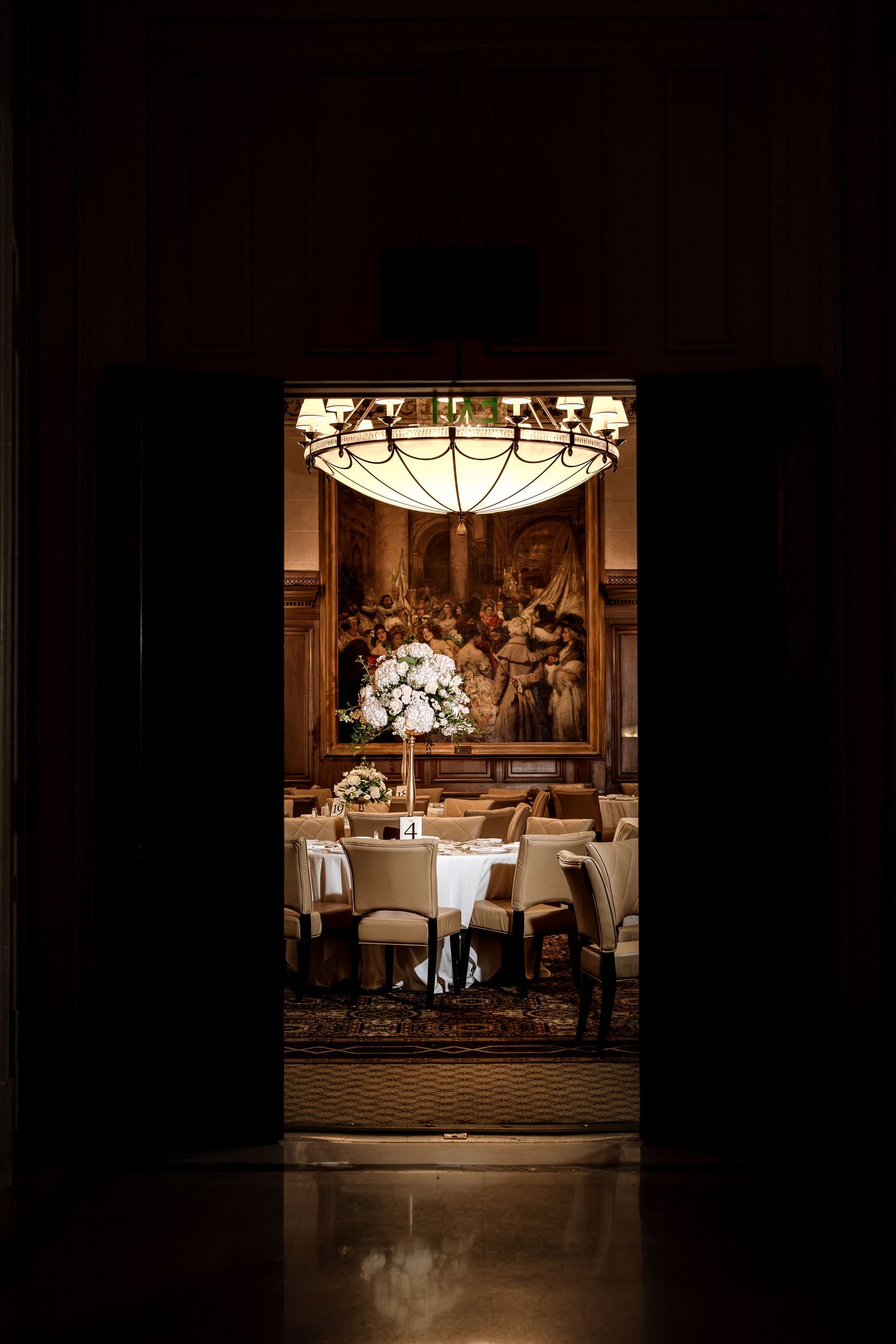 Dramatic doorway view of an elegant wedding reception room with chandelier and floral centerpiece.