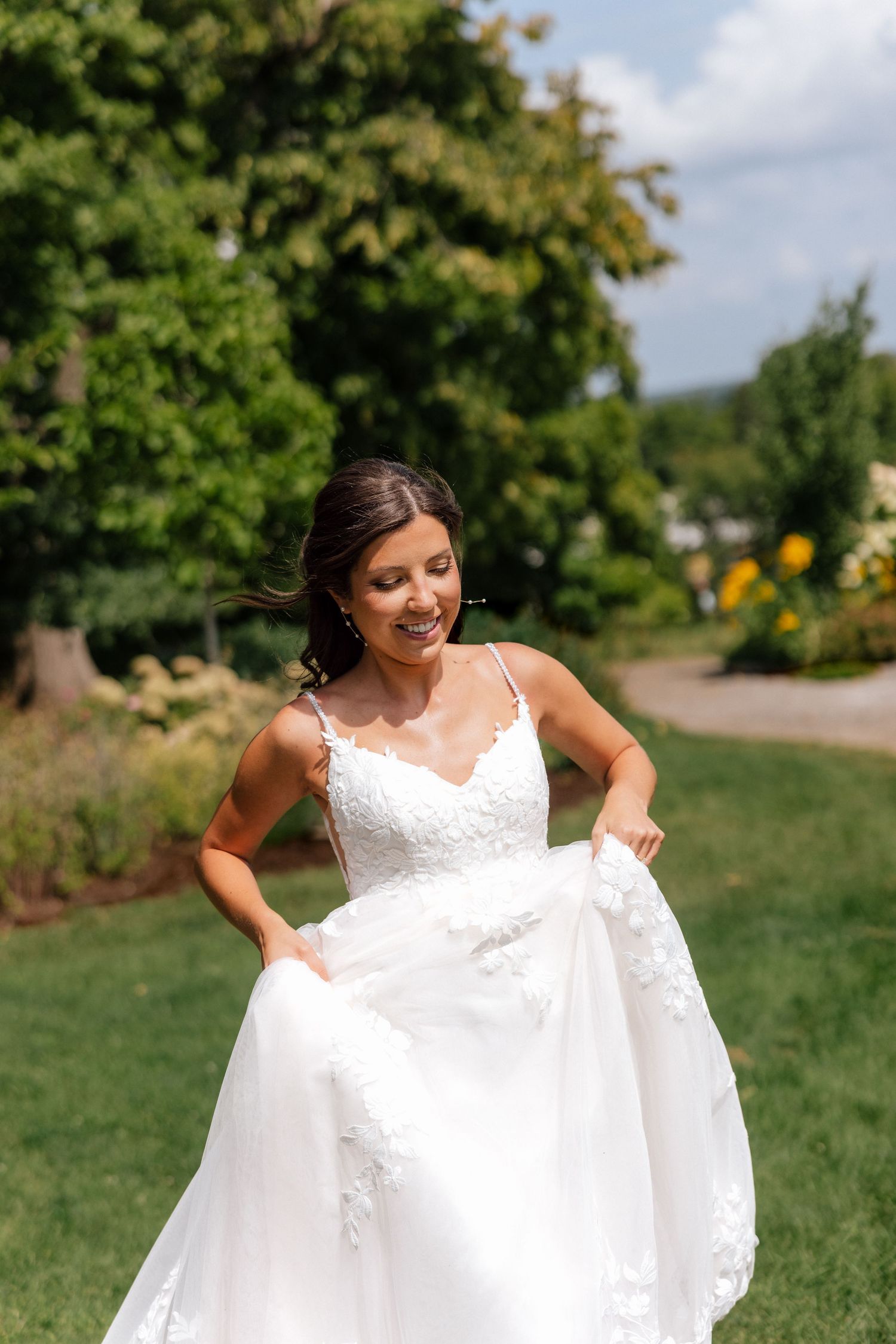 Smiling bride in lace A-line wedding dress twirling in a lush green garden setting.