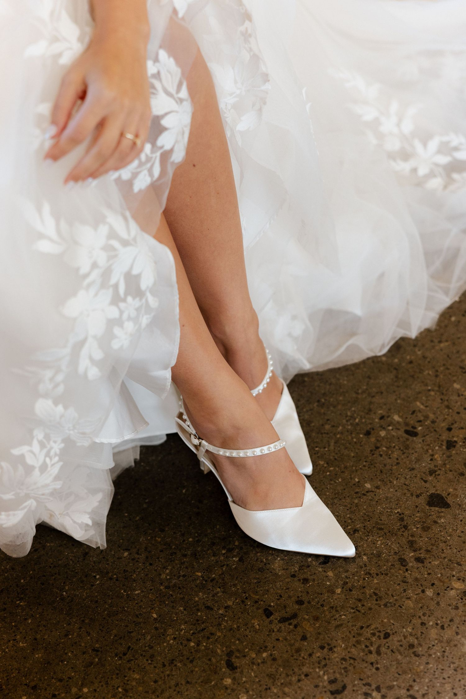 Bride wearing white pointed-toe heels with pearl ankle strap detail and lace wedding gown.